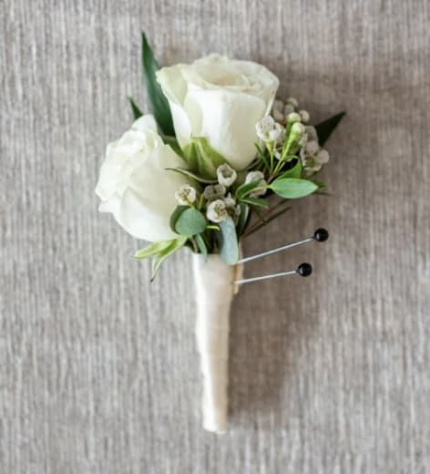 White rose boutonniere with small white filler flowers wrapped in ivory ribbon.