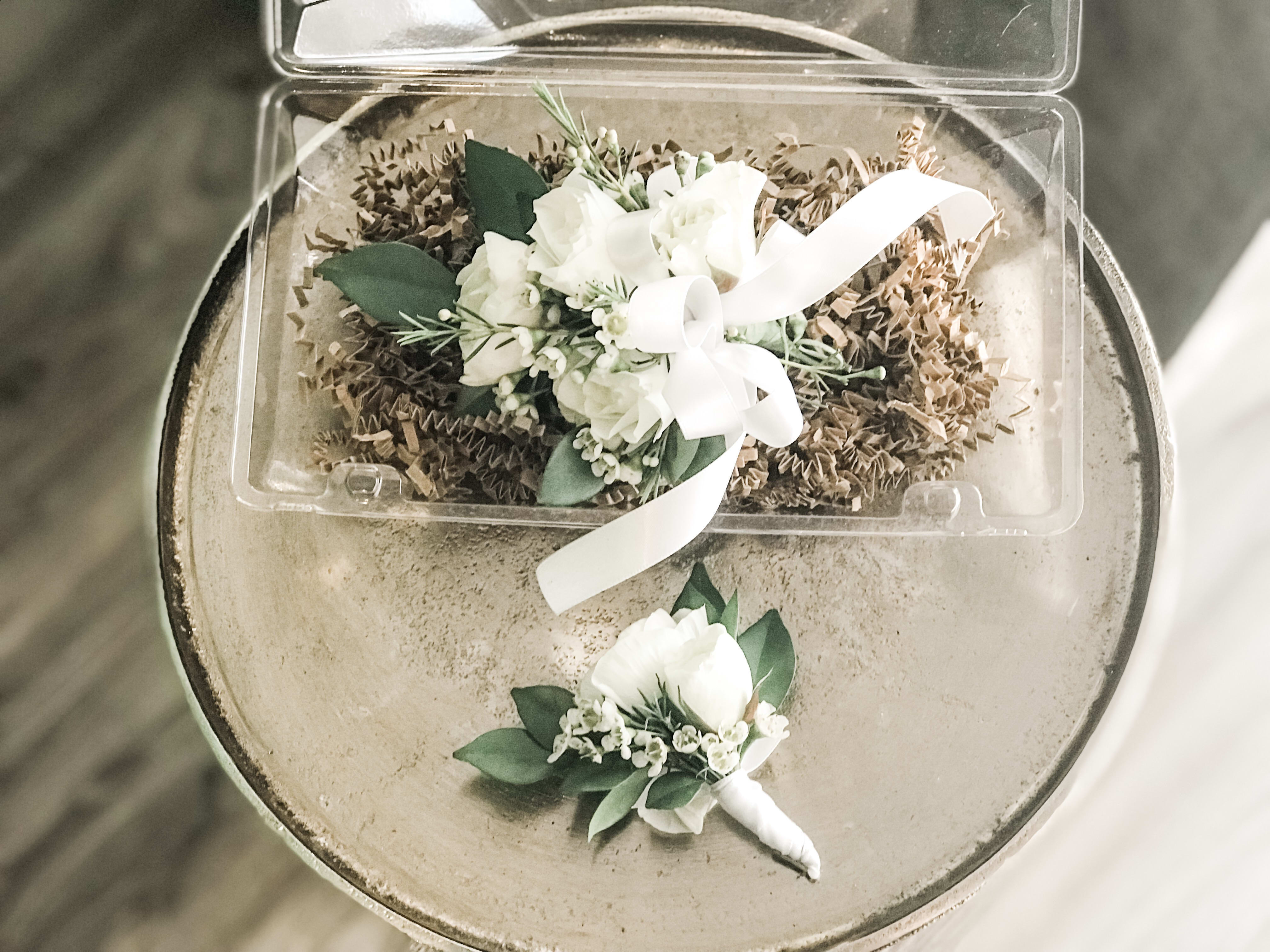 White rose wrist corsage with matching boutonniere on a round table