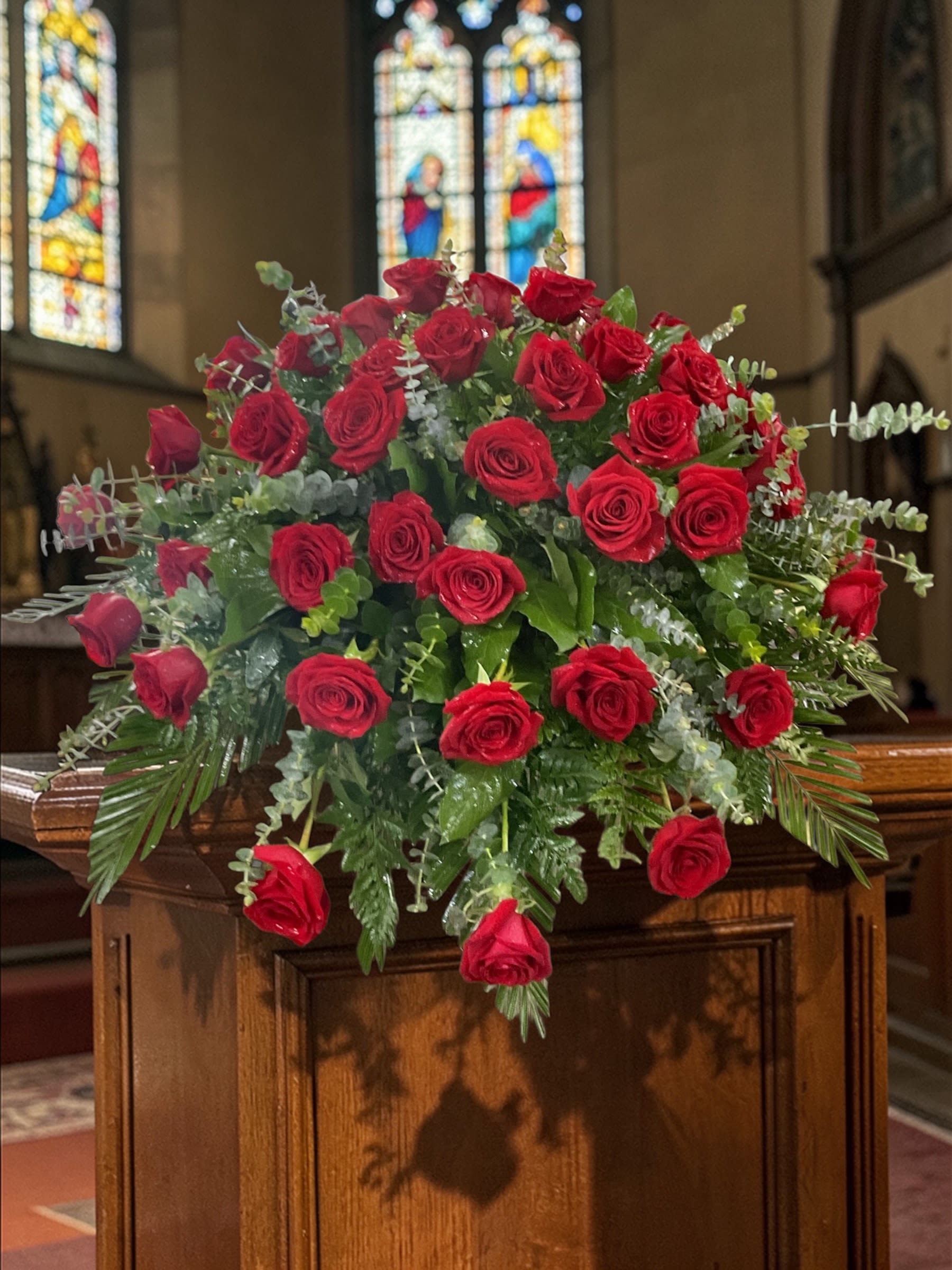 Majestic Red Casket Spray - Majestic Red is a classic casket spray built around the power and simplicity of rich red roses, accented with fresh eucalyptus and layered greenery for natural depth and balance.  The design focuses on unity and presence. A strong, uninterrupted field of red creates immediate visual impact, while the greenery adds soft movement and framing without pulling attention away from the roses.  Chosen by families who want something timeless, heartfelt, and visually striking without unnecessary embellishment, this all-red rose tribute carries its message clearly and confidently.  Arranged to rest beautifully across the casket, it offers structure, fullness, and a clean silhouette that reads well from every angle during visitation and funeral services.  Each arrangement is created with the freshest stems available. Subtle variations may occur while preserving the overall look and color.  Available for casket flower delivery through Aspen Tower Florist, serving Shelbyville and Greensburg along with Rushville, Batesville, Westport, Oldenburg, St. Paul, Waldron, Milroy, and Hope.