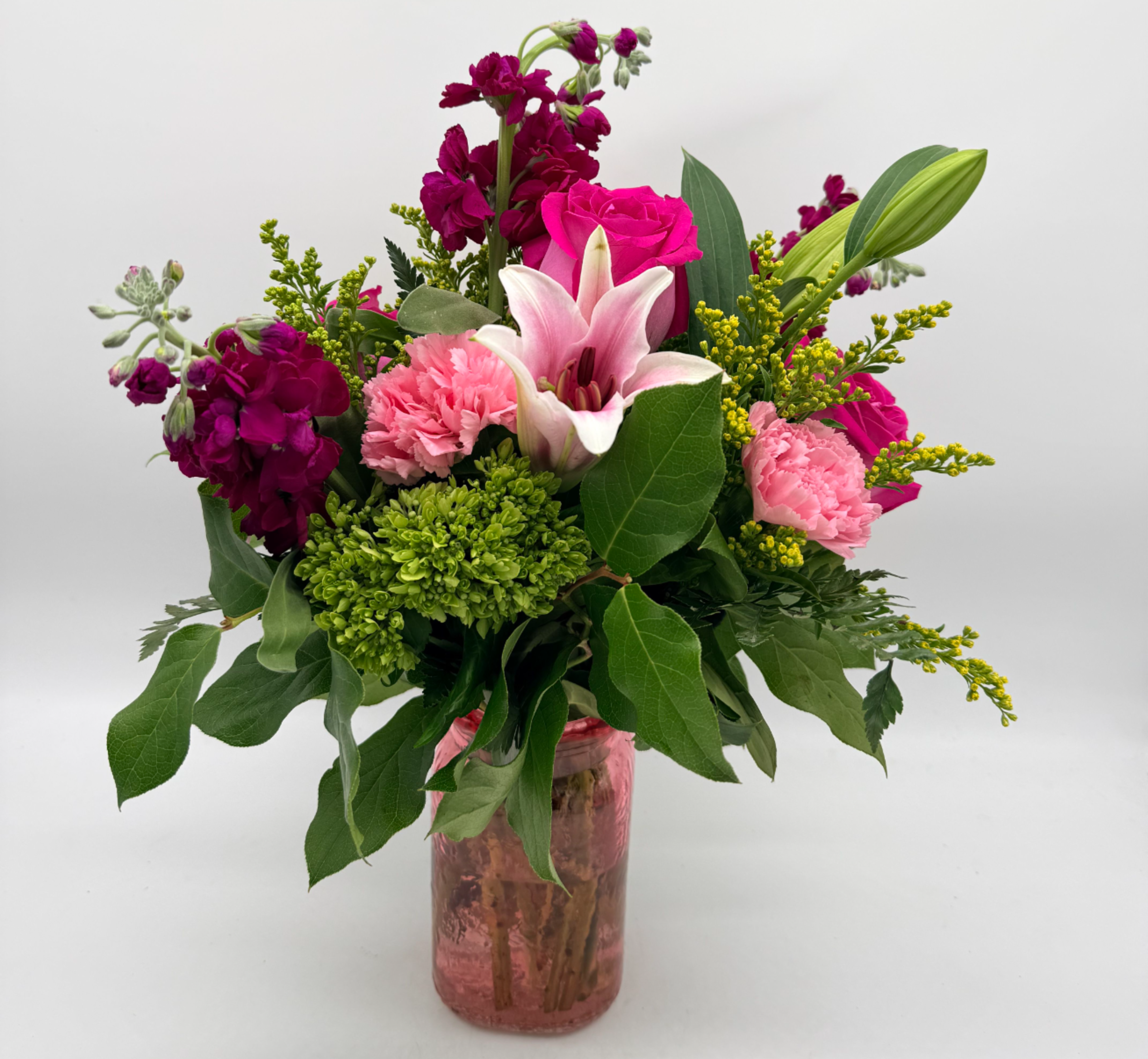 Sweet Raspberry - Fun, flirty, and full of color, this bouquet showcases roses, a lily, carnations, and accent blooms in vibrant tones. Designed in a pink glass vase with fresh greenery. Flower varieties and shades may vary.