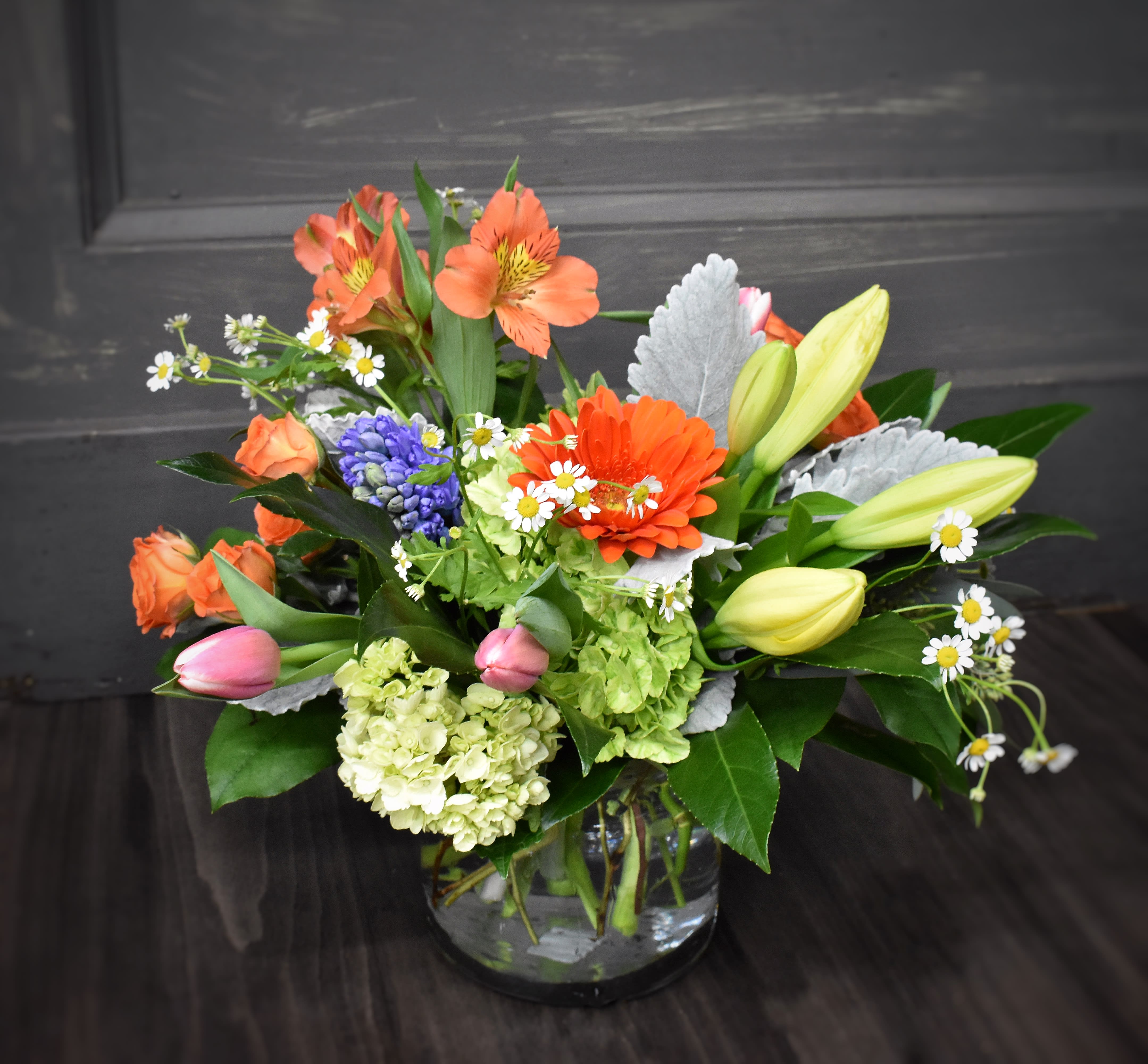 Mixed bouquet with orange blooms, lilies, and daisies in a glass vase
