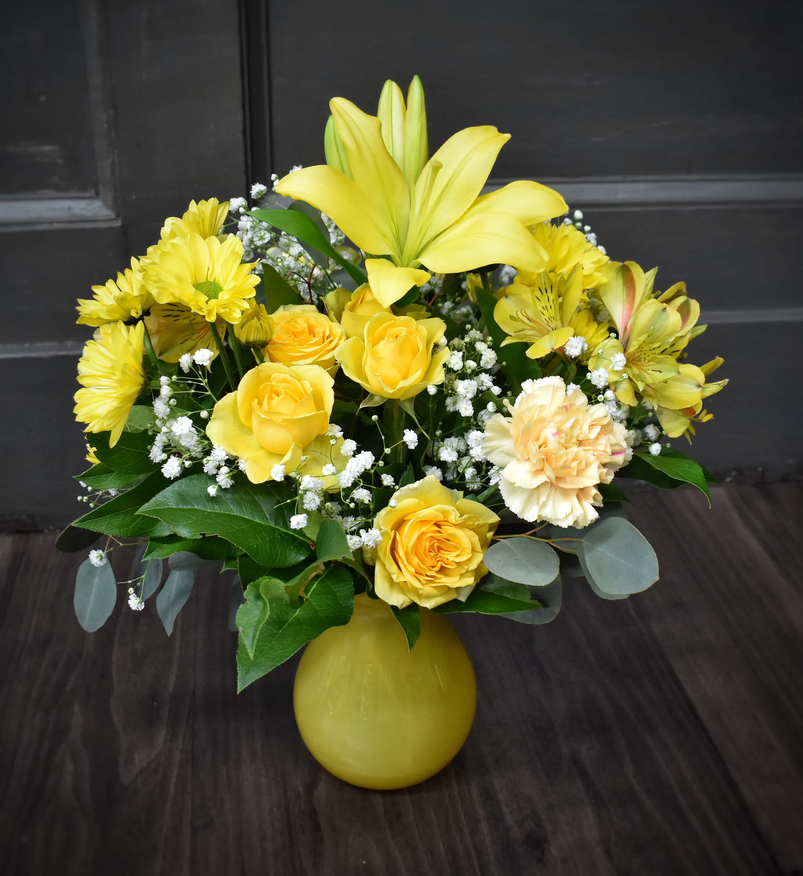 Yellow roses and lilies arranged in a yellow vase
