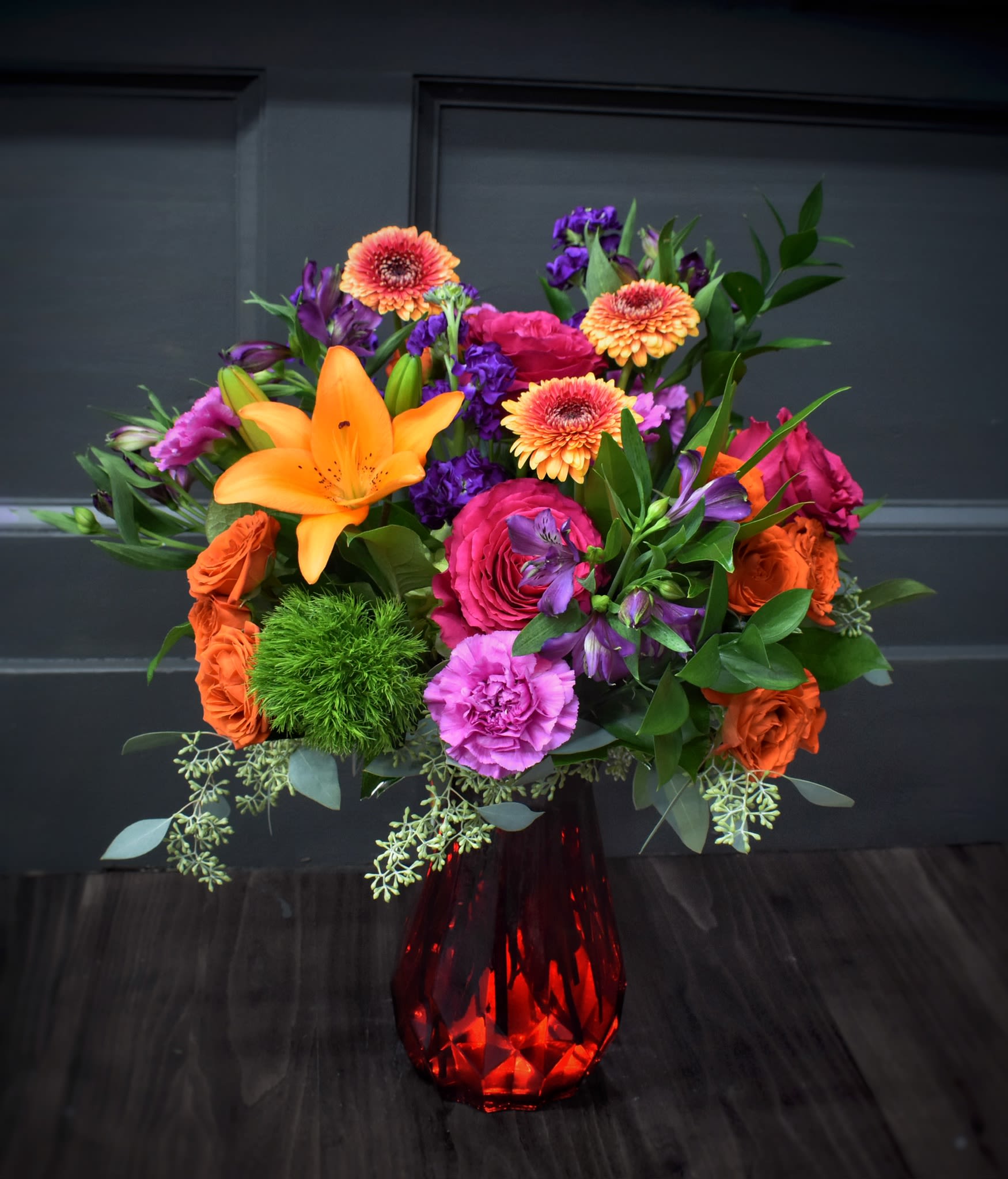 Bright mixed bouquet in a red glass vase with orange, pink, and purple flowers.