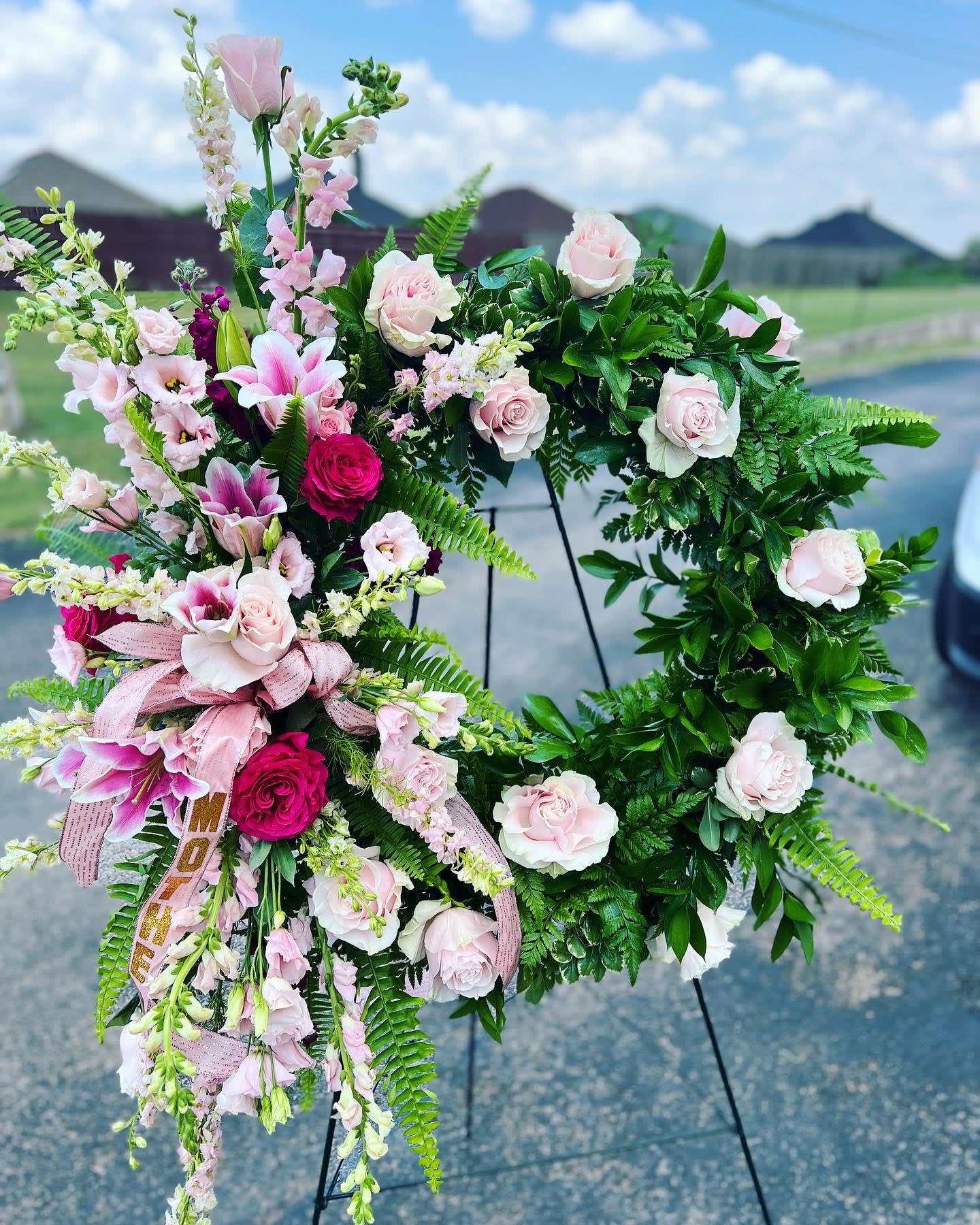 Pink and white floral wreath on a stand with ribbon accents