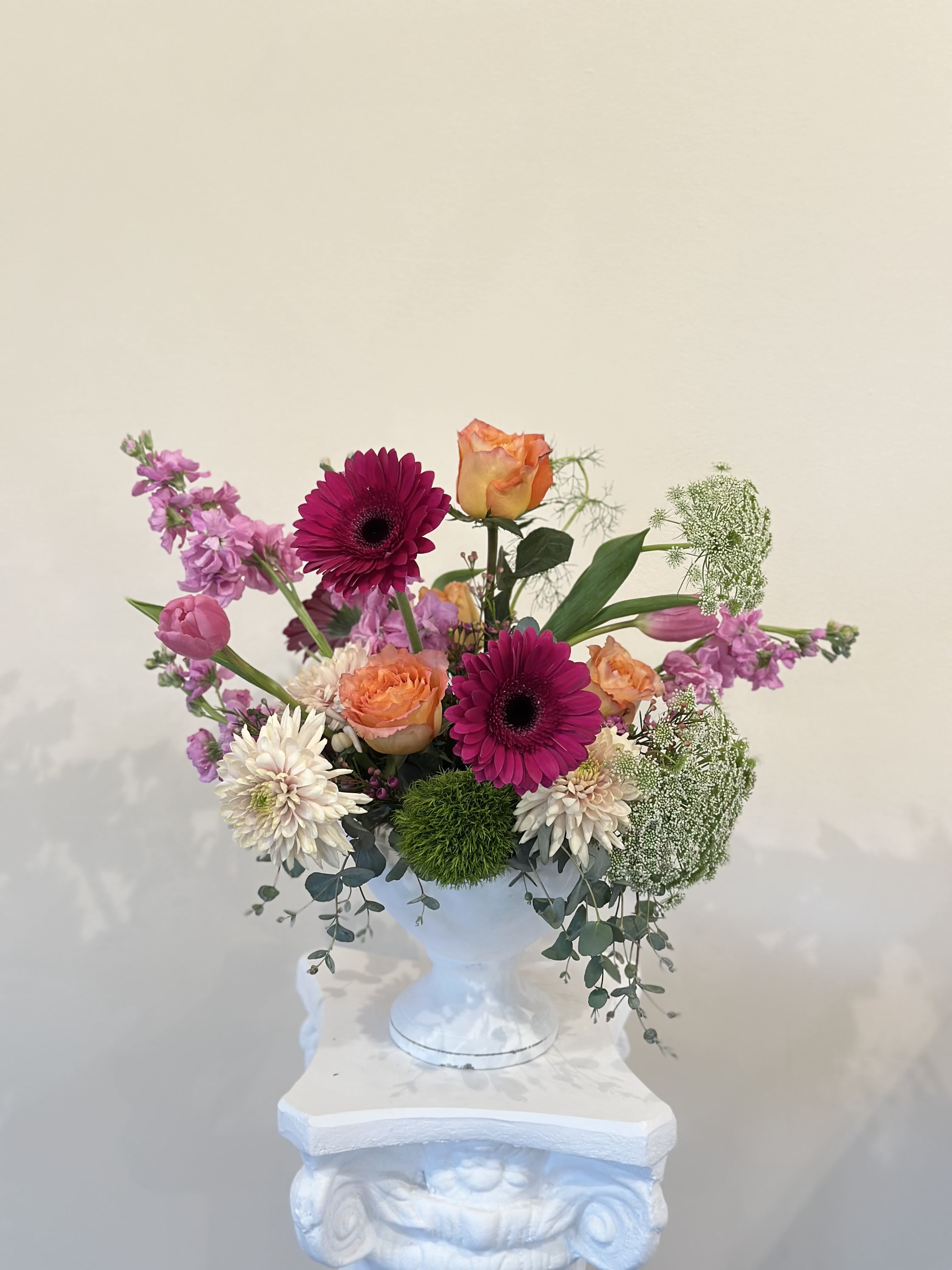 Mixed bouquet in a white pedestal vase with pink, orange, and white blooms