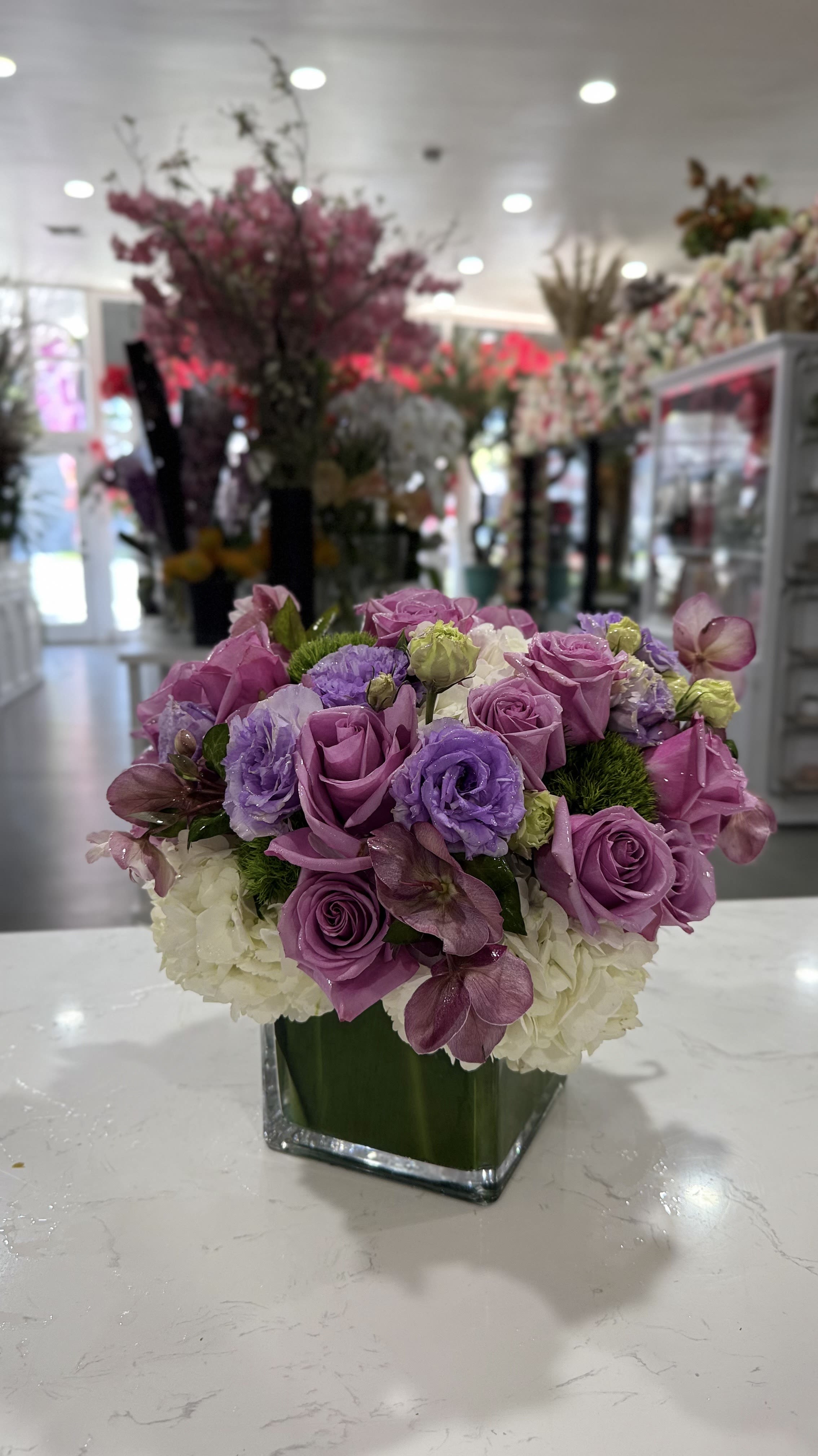 Purple roses and hydrangeas arranged in a square glass vase
