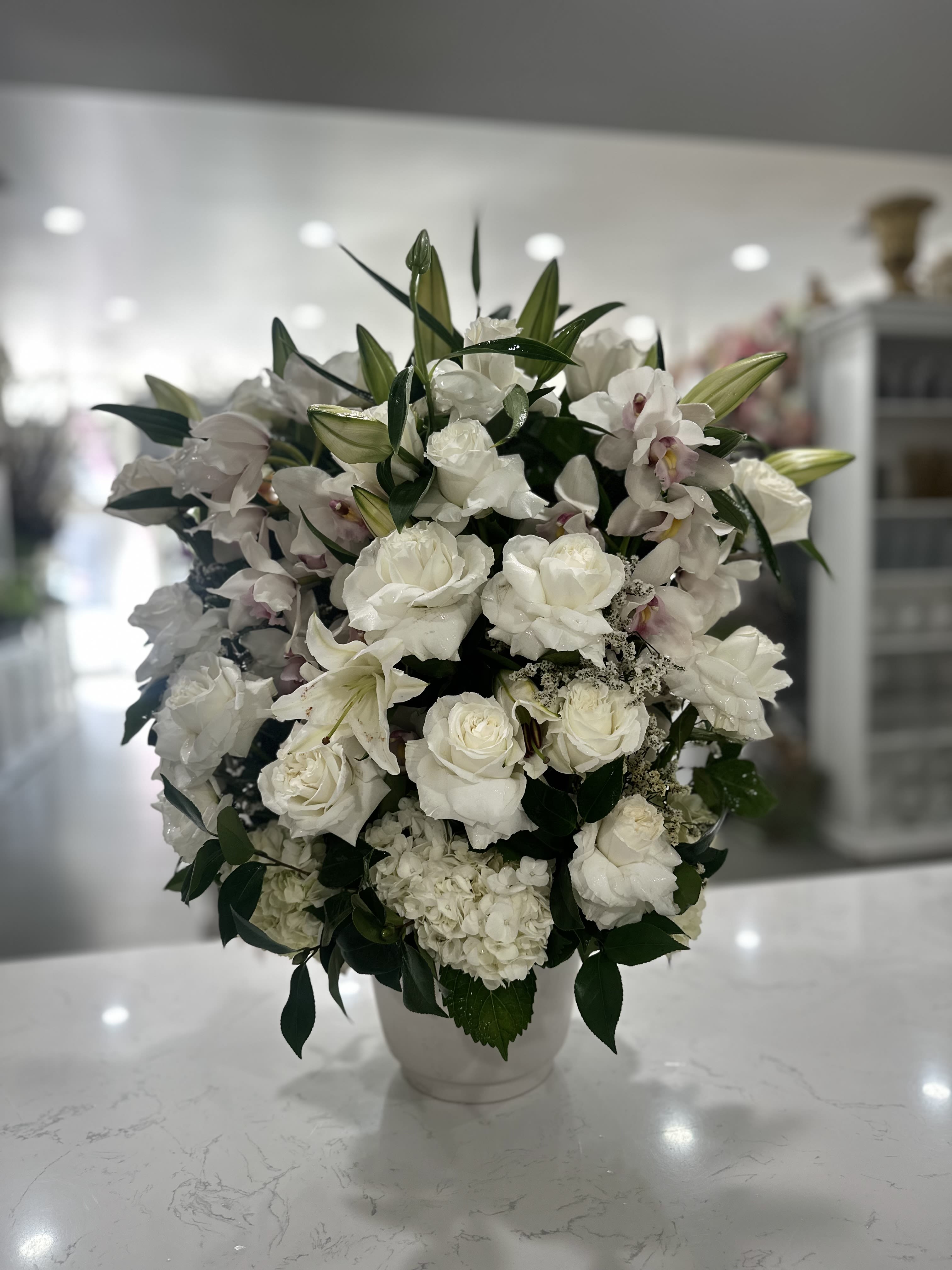 White floral arrangement in a white vase with roses and lilies