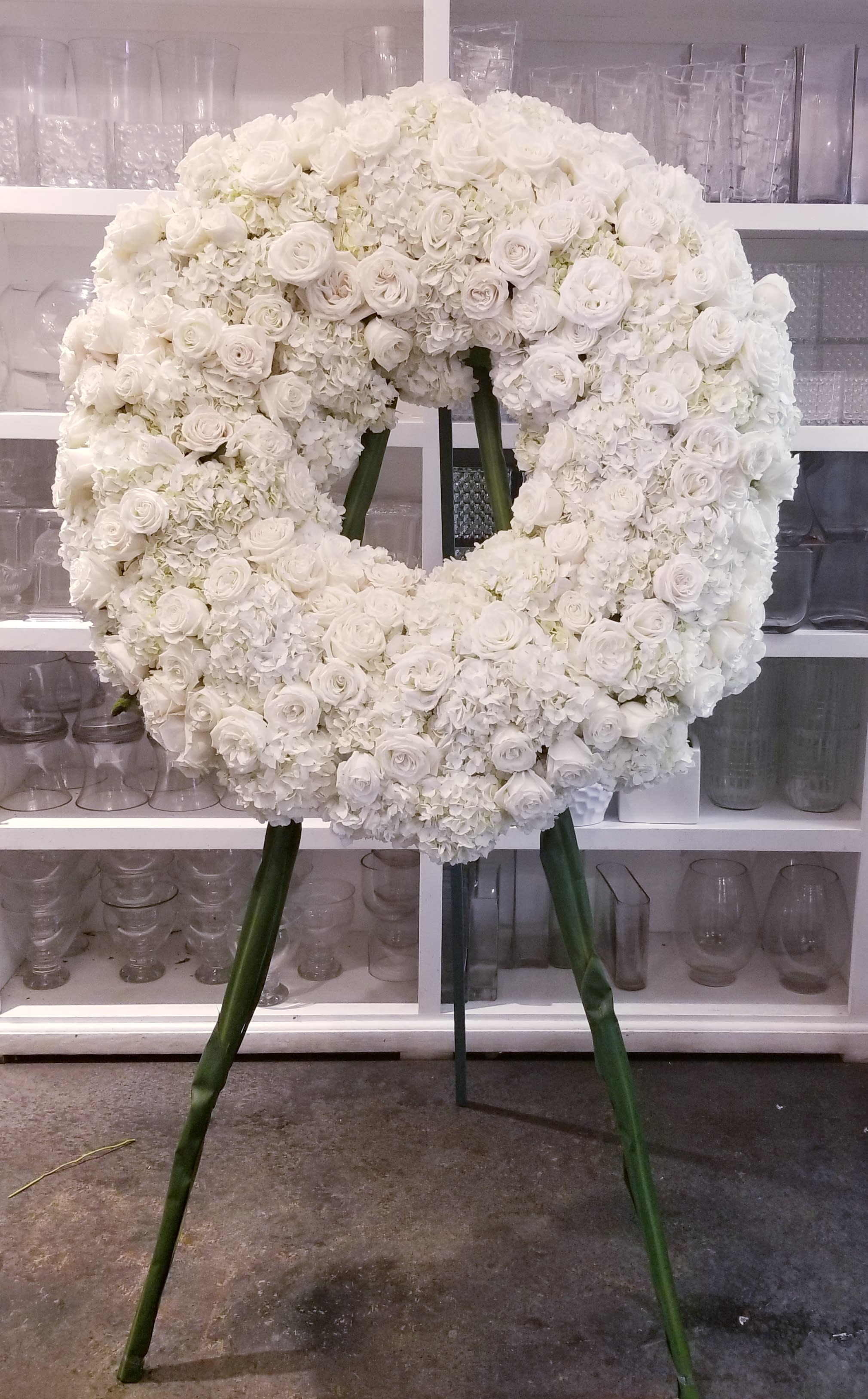 Large white floral wreath on a stand with roses and hydrangeas