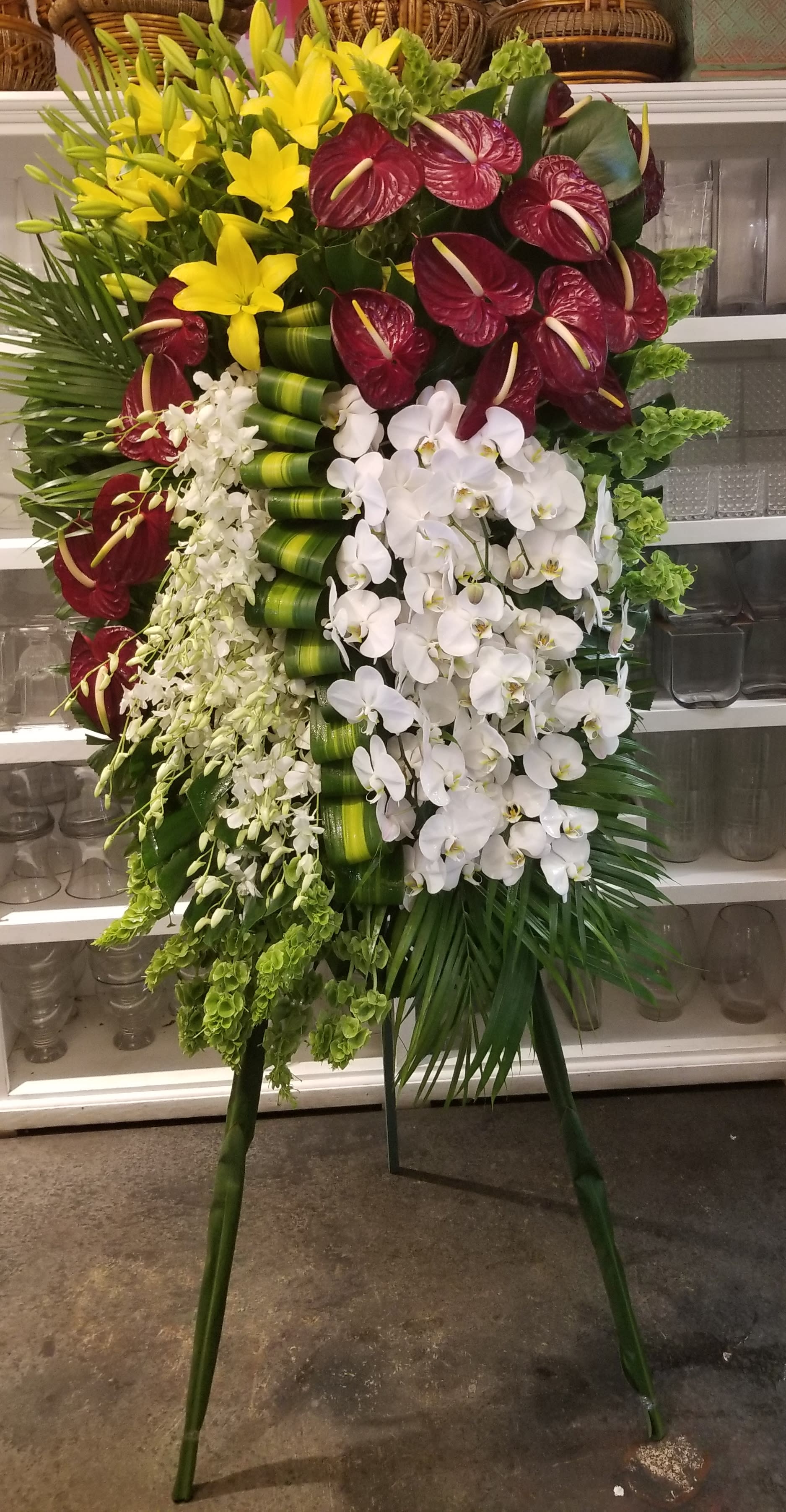 Tall standing floral spray with yellow lilies, burgundy anthuriums, and white orchids