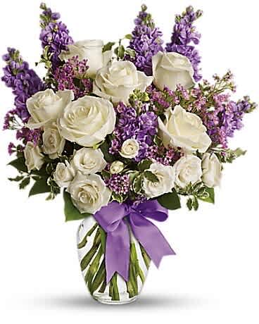 White roses and purple flowers in a clear glass vase with a purple ribbon