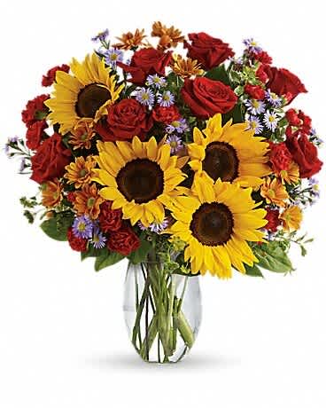 Bouquet of sunflowers, red roses, and small purple flowers in a glass vase