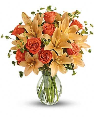 Orange roses and pale lilies in a clear glass vase