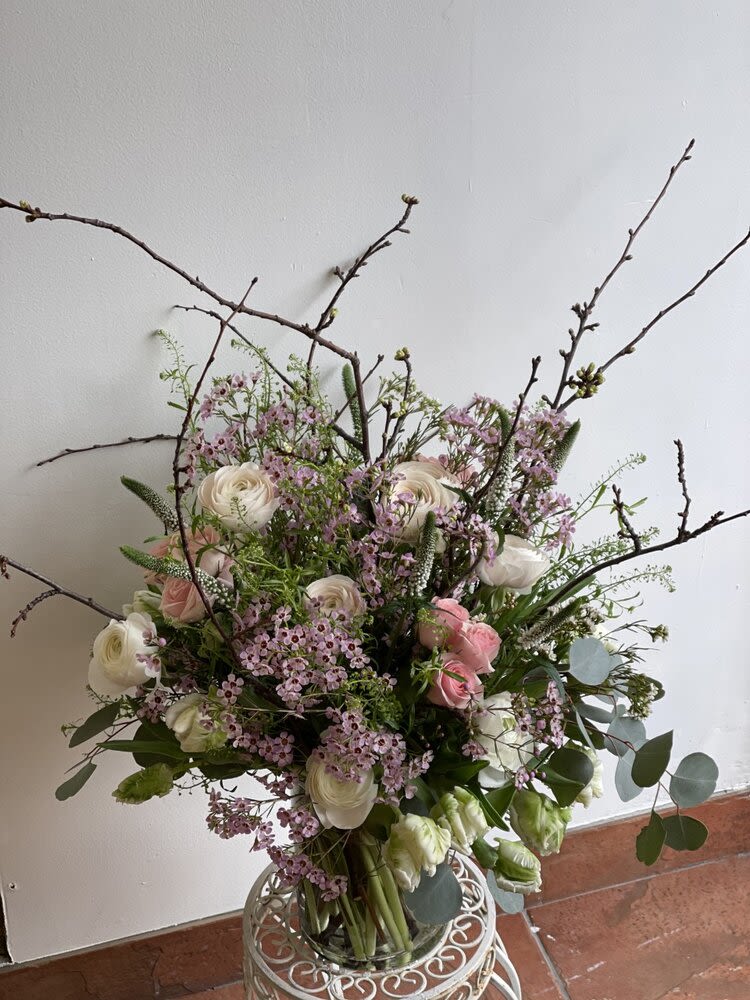 Tall bouquet of white and pink flowers with branching twigs in a glass vase
