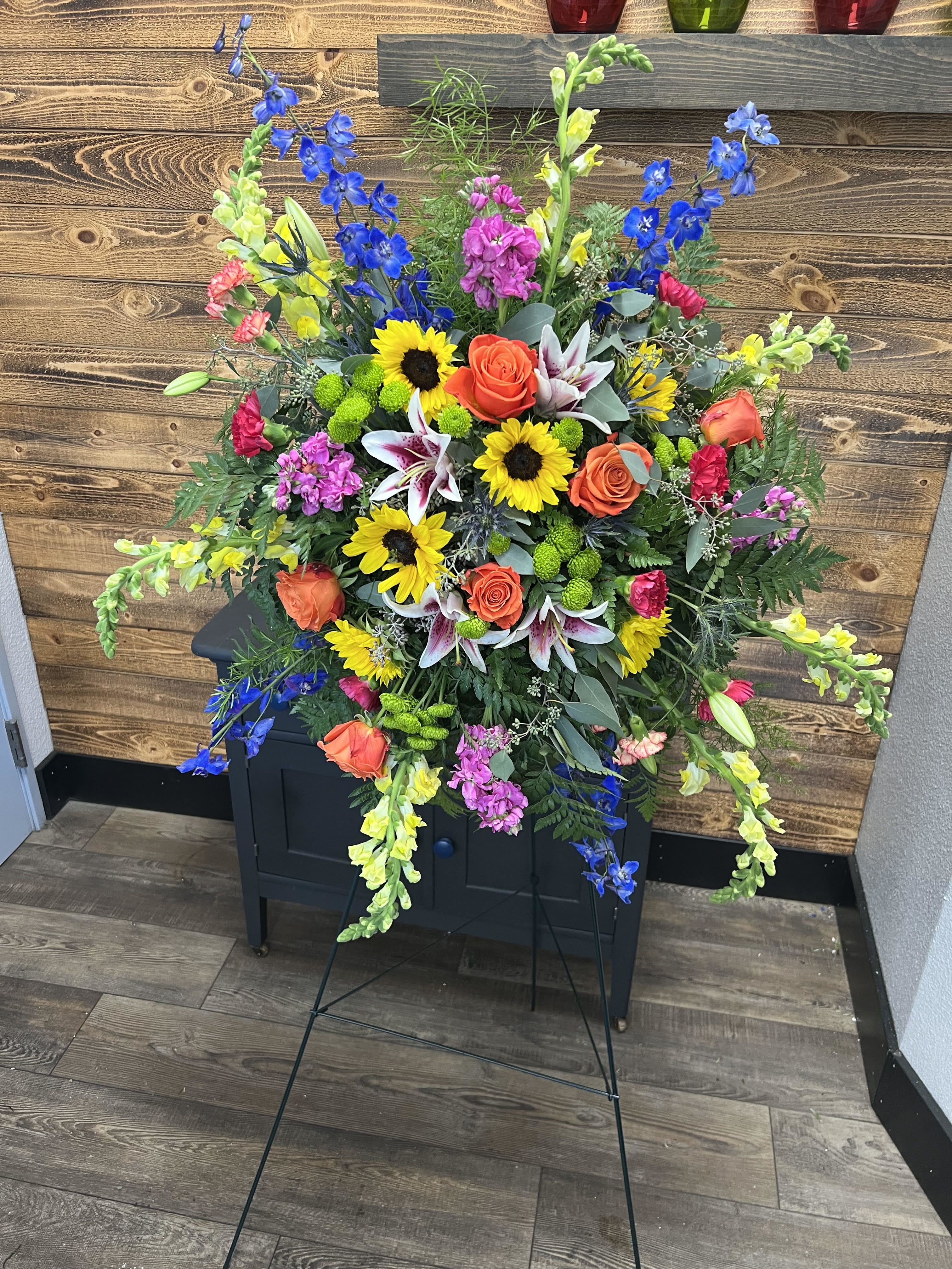 Large standing floral spray with sunflowers, roses, lilies, and blue delphinium
