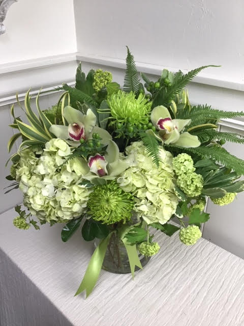 Green floral arrangement with orchids and hydrangeas in a glass vase