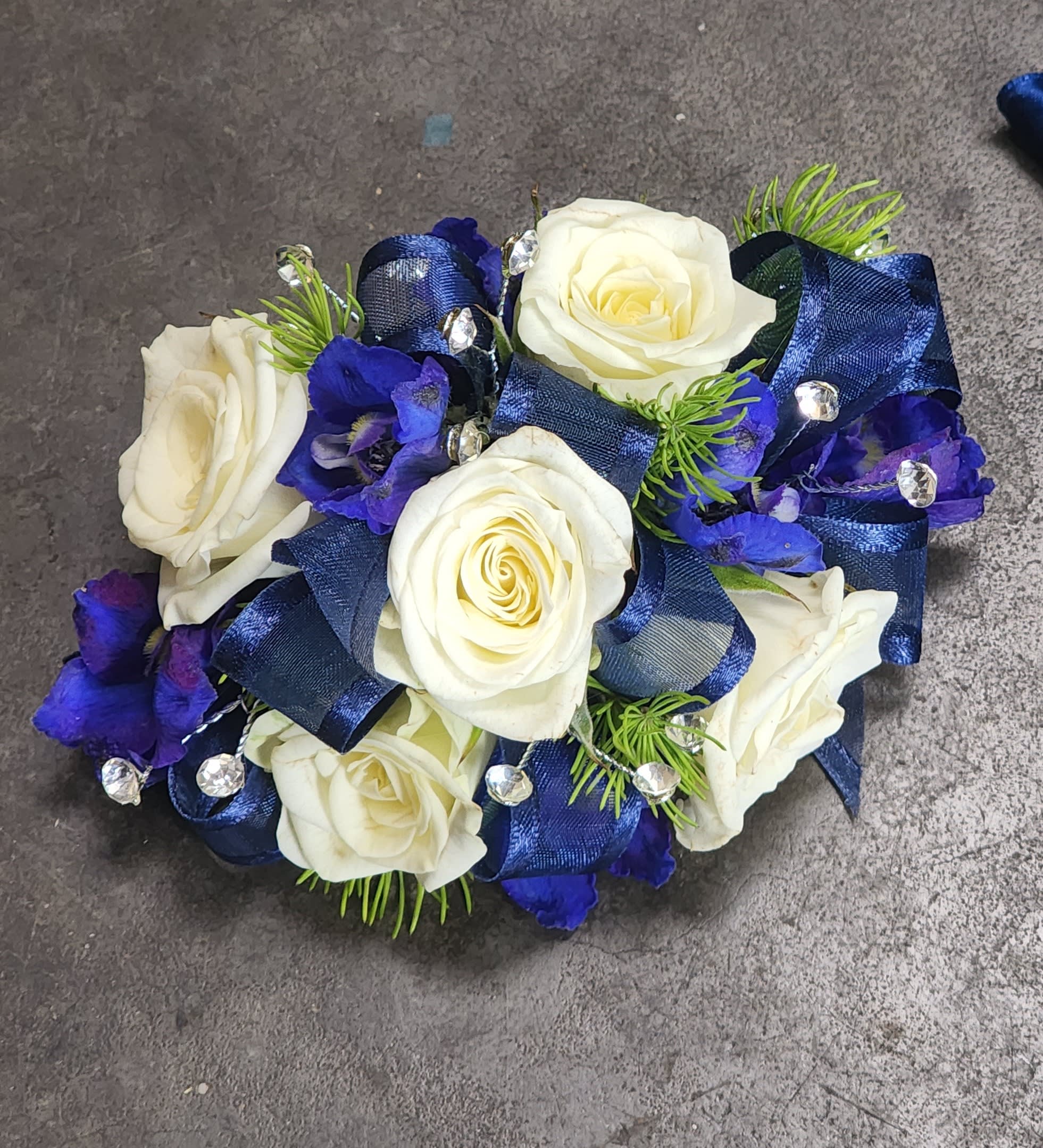Blue Elegance Wristlet - A wrist corsage of white spray roses, dark blue belladonna, dark blue ribbon &amp; clear rhinestones.  Depending on availability of ribbon, may change slightly.