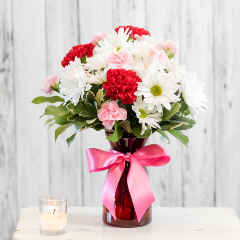Bouquet of white daisies and red carnations in a red vase with a pink ribbon