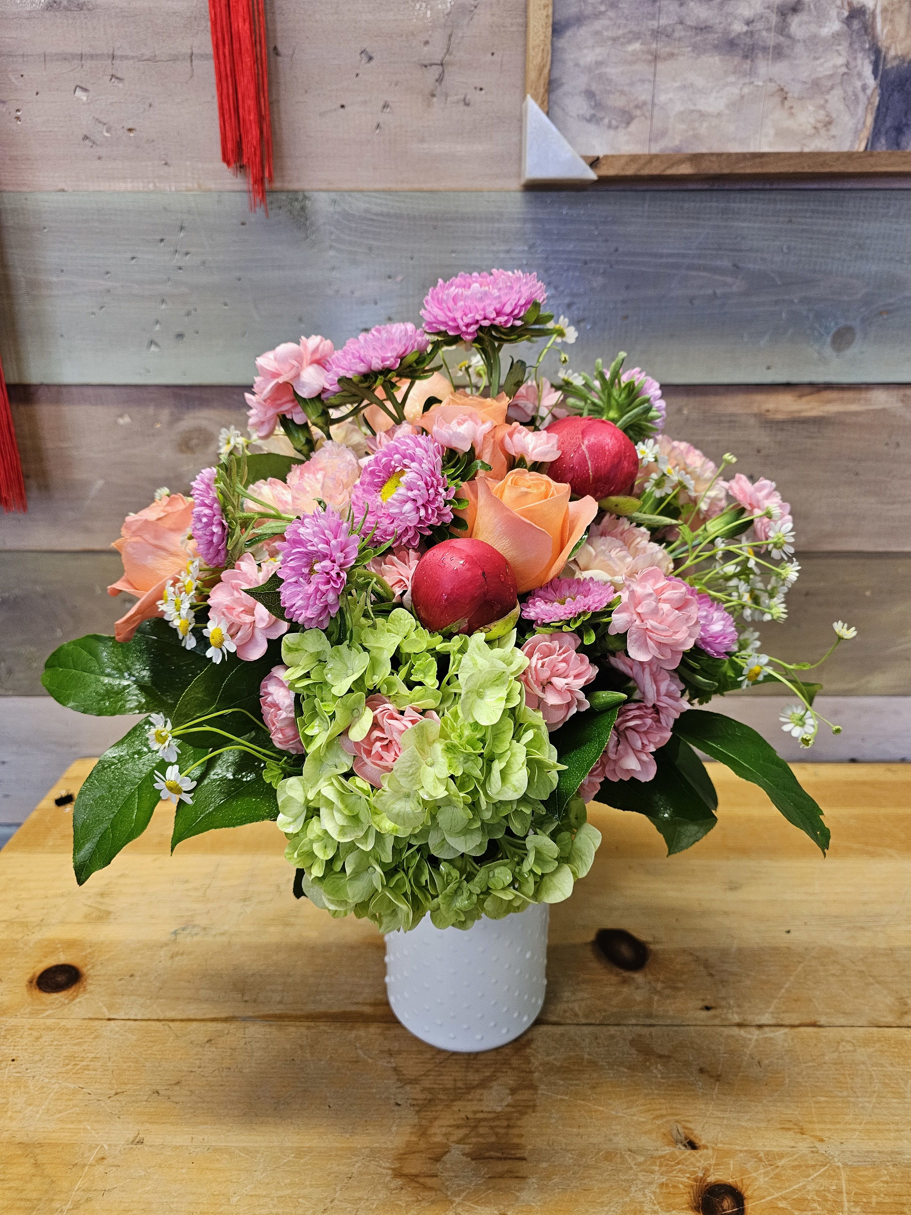 Pink and peach bouquet in a white vase with green hydrangea and red ornaments