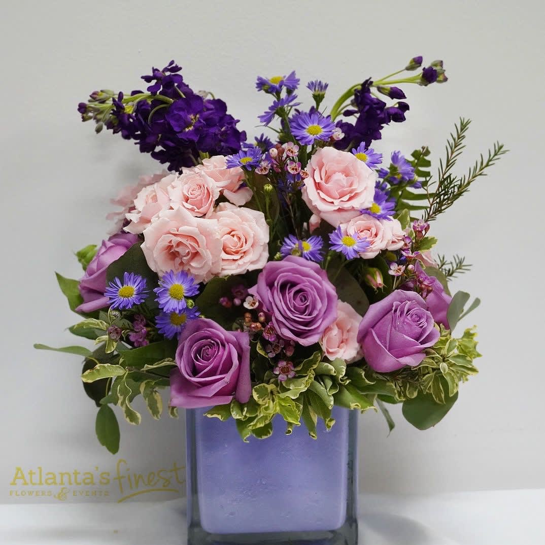 Lavender Bouquet by Atlanta's finest flowers - A lush mix of large white roses, blush pink spray roses, and vivid purple blooms creates a feminine, cheerful bouquet perfect for a Mother's Day gift, birthday, or a thoughtful "just because" surprise. The compact, rounded design pairs soft pastels with saturated lavender and purple accents so the recipient will feel genuinely seen-cheered, comforted, or celebrated-whether you're sending thanks, well-wishes, or congratulations.  This flower arrangement includes roses, spray roses, asters, stock, daisies, carnations and complementary filler in pink, purple, lavender and white, artfully arranged for texture and contrast. It arrives in a clear square glass vase with a purple-tinted water insert that reinforces the palette and gives a polished, decorative finish. Sized as a lush, hand-delivered bouquet, it's equally suited for spring and summer occasions like Easter or Passover and special moments such as Women's Day, Best Friends Day, or Admin Professionals' Week; gentle care-fresh water and a cool spot-will keep blooms looking their best.