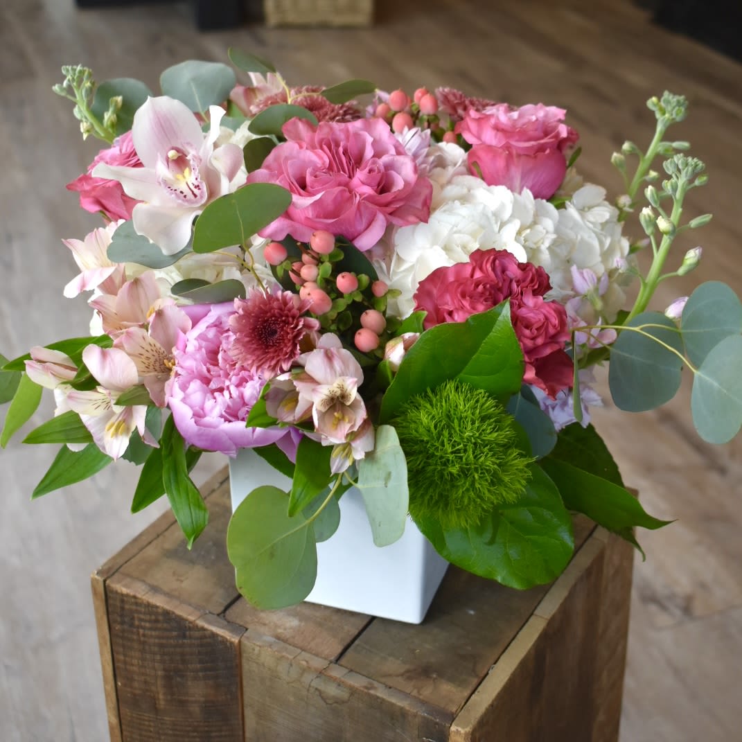 She Deserves It All - She Deserves it All is a composition of white hydrangea, hot pink roses, peonies, pink orchids, stock, hypericum, and dianthus in an elegant linen cube. 