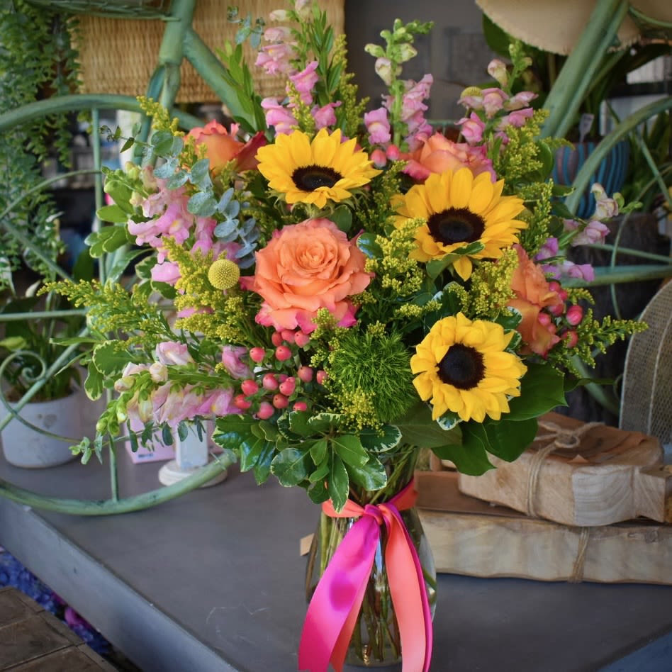 She Deserves To Be Celebrated - Show your appreciation with our bright and tall composition of sunflowers, free spirit roses, pink snapdragons, craspedia, hypericum, dianthus, and solidago in a 9” Jordan vase. 