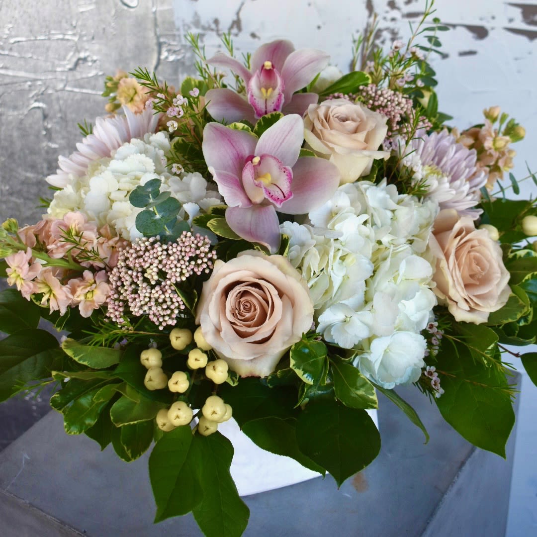 She Deserves All The Love - A cascade of timeless blush hues, She Deserves All The Love contains white hydrangea, quicksand roses, pink orchids, pink fairytale cremons, peach stock, pink rice flower, pink wax flower, and white hypericum in a linen cube.