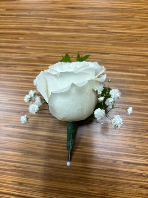 White rose boutonniere with baby's breath on a wooden surface