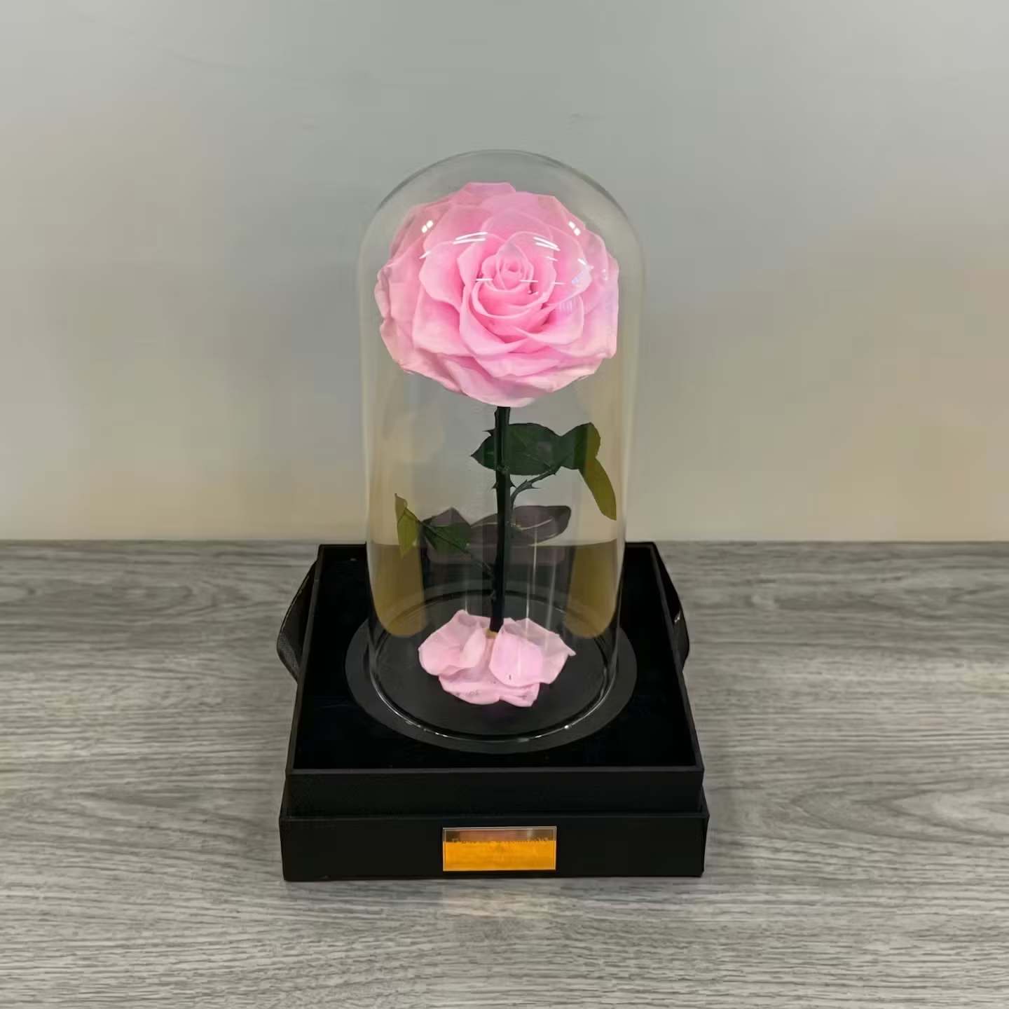 Beauty and the beast Pink - A single soft-pink rose preserved beneath a clear glass dome creates an instantly romantic keepsake - perfect as an anniversary or Valentine's Day gift, a Mother's Day surprise, or a "just because" gesture that will keep giving. The contrast of the delicate layered bloom against the black display base gives the piece a formal, museum-like presence that also suits birthdays, graduations, or a thoughtful get-well or sympathy gift.  The rose is natural and long-lasting, presented in a clear glass cloche set on a black presentation base with a few loose pink petals thoughtfully arranged at the bottom. The arrangement sits inside a clear plastic container for safe delivery and display; the compact footprint makes it easy to place on a nightstand, desk, or mantel as a lasting reminder of the occasion.  Designed to endure, the preserved rose requires no water or special care and will retain its look for approximately three years, making it an elegant choice for holidays, Mother's Day, Father's Day, anniversaries, prom, Christmas, or as a new baby or congratulations keepsake.