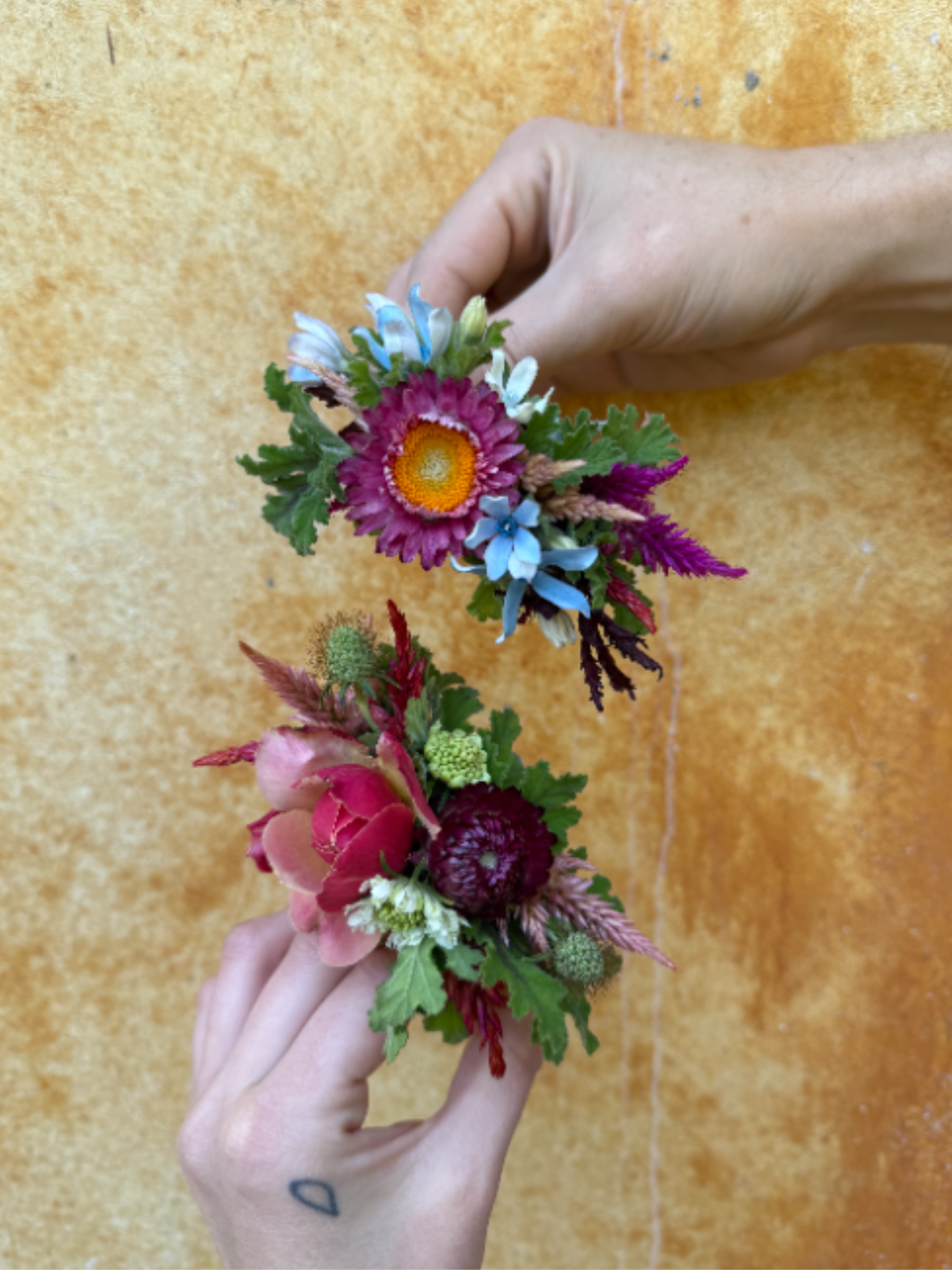 Two small floral wrist corsages held in hands against a warm background