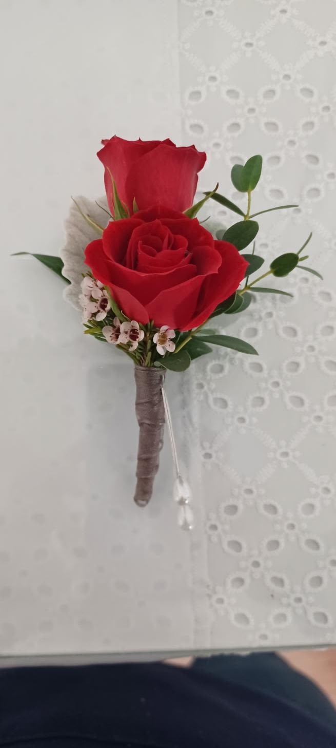 boutaneer - Two red roses form a compact, romantic focal point in this boutonniere-one fully open and one gently cupped-making it an ideal boutonniere for weddings, proms, or any dress-up occasion where classic style matters. Small white accent blossoms and fresh green sprigs provide soft contrast and delicate texture so the person you're honoring will look polished and thoughtfully styled.  Stems are tightly wrapped in a neat boutonniere wrap and finished with a clear floral pick for secure attachment to lapels or corsages. The low-profile design keeps the flowers close to the chest for photos and comfort; colors are rich red, crisp white, and lively green to coordinate with traditional formalwear palettes.  Hand-delivered for same-day events when available, this boutonniere is meant to make the wearer feel recognized and celebrated-order to match boutonnieres with bouquets or corsages for a cohesive look. Handle gently, keep cool, and mist lightly to preserve freshness before the event.