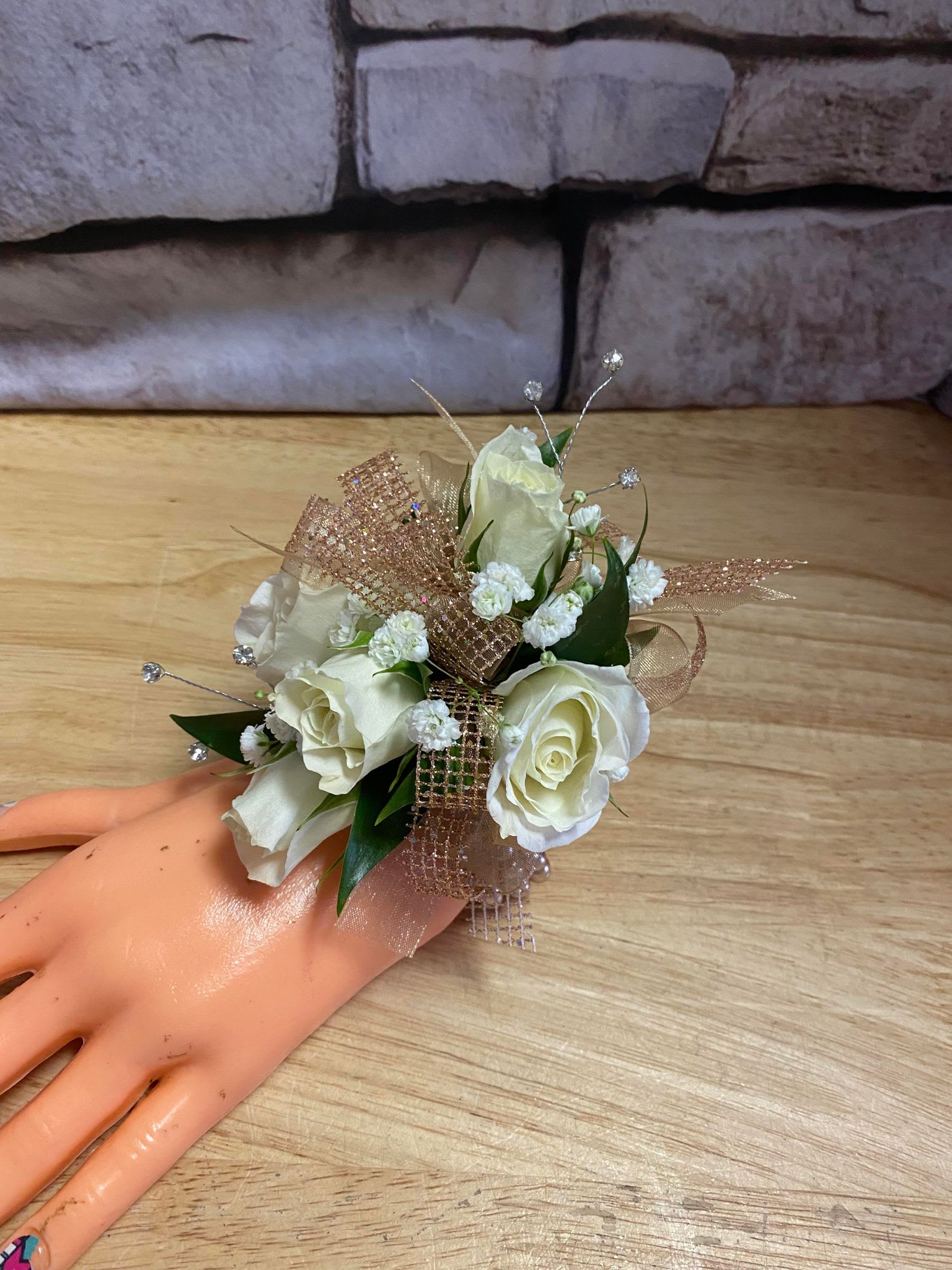 White rose corsage with gold ribbon on a mannequin hand