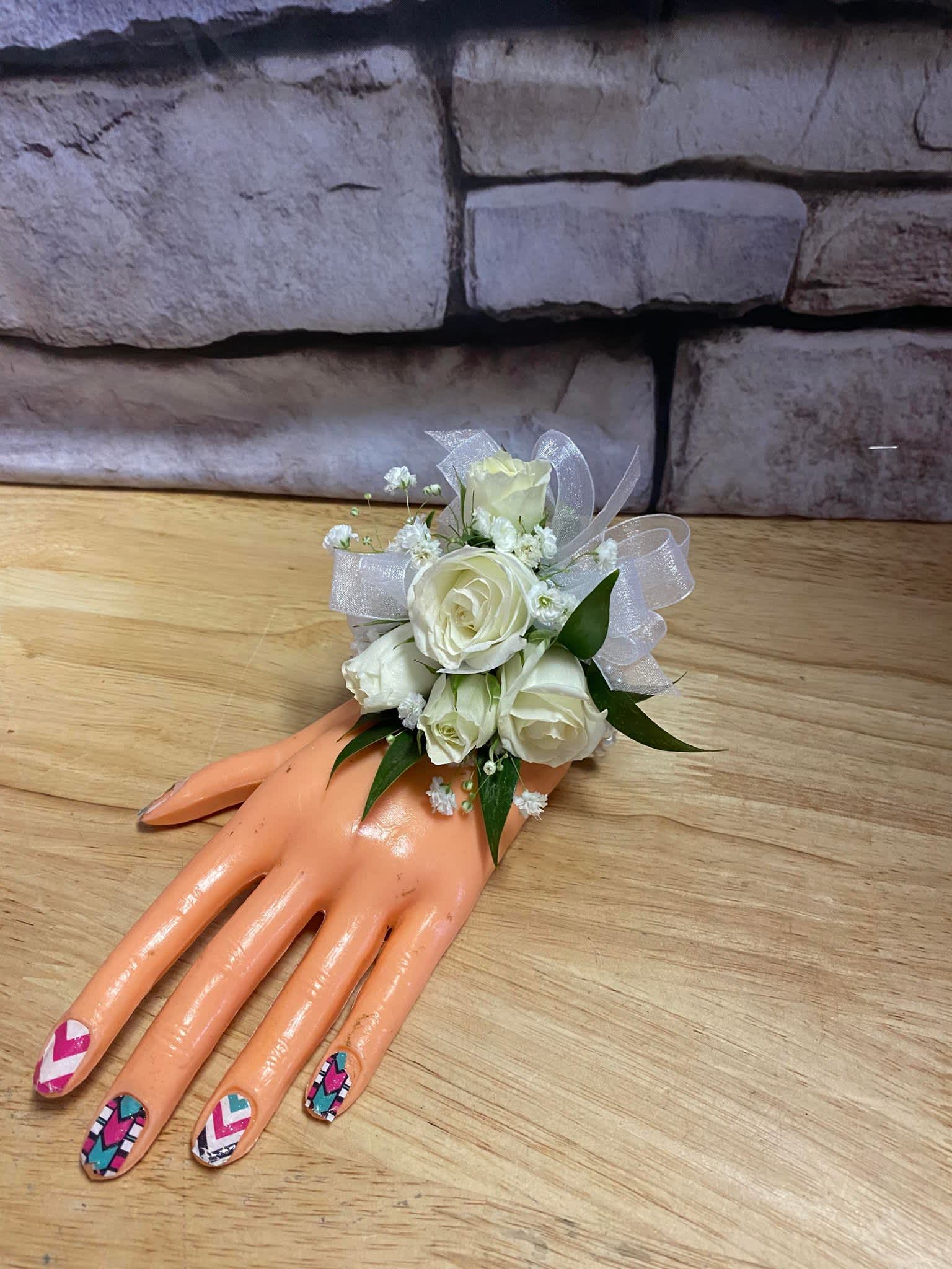 White rose wrist corsage on a mannequin hand with sheer ribbon