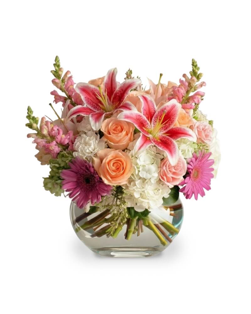 Radiance for Mom - A joyful burst of color and fragrance, this Mother’s Day bouquet celebrates her with a symphony of blooms. Warm coral roses and soft blush spray roses mingle with the playful pop of fuchsia gerbera daisies, while lush white hydrangeas bring a grounding elegance. Pink oriental lilies open in graceful arcs, complemented by clusters of purple stock and lilac-hued blooms for a touch of serenity. This design is finished with delicate sprays of pink waxflower, creating a lush, garden-fresh arrangement that mirrors the beauty and love she shares every day.  As similar as possible. Designer may make substitutions based on flower availability. 