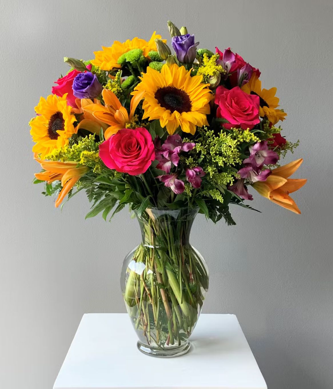 Sunshine Delight Bouquet - Bright, joyful, and full of life — the Sunshine Delight Bouquet brings instant happiness to any space. Bursting with golden sunflowers, vibrant pink roses, striking orange lilies, and hints of purple blooms, this lively arrangement celebrates color and cheer. Presented in a classic glass vase, it’s the perfect gift to uplift someone’s day, celebrate special moments, or simply add a radiant touch to your home.