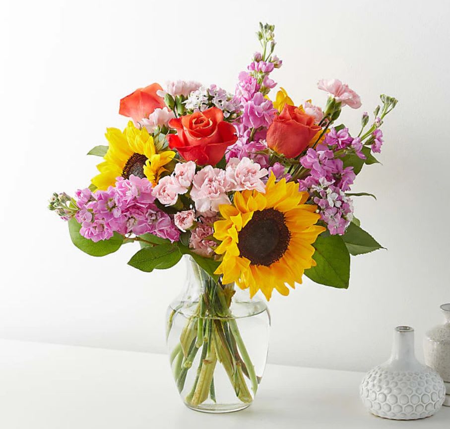 Sunshine &amp; Charm Bouquet - Bring warmth and happiness to any moment with our Sunshine &amp; Charm Bouquet, a radiant design that celebrates life with every bloom. Crafted with care by our expert florists in The Bronx, NY, this bouquet bursts with color and personality.  A cheerful mix of bright sunflowers, vibrant orange roses, soft pink carnations, and lavender stock blossoms, all arranged in a sleek clear glass vase. The combination of yellow, orange, pink, and lavender tones creates a joyful and elegant harmony—perfect for birthdays, congratulations, thank-you gifts, or simply to brighten someone’s day.  Each bouquet is freshly designed and available for same-day delivery, ensuring that your thoughtful gesture arrives with stunning beauty and lasting freshness.