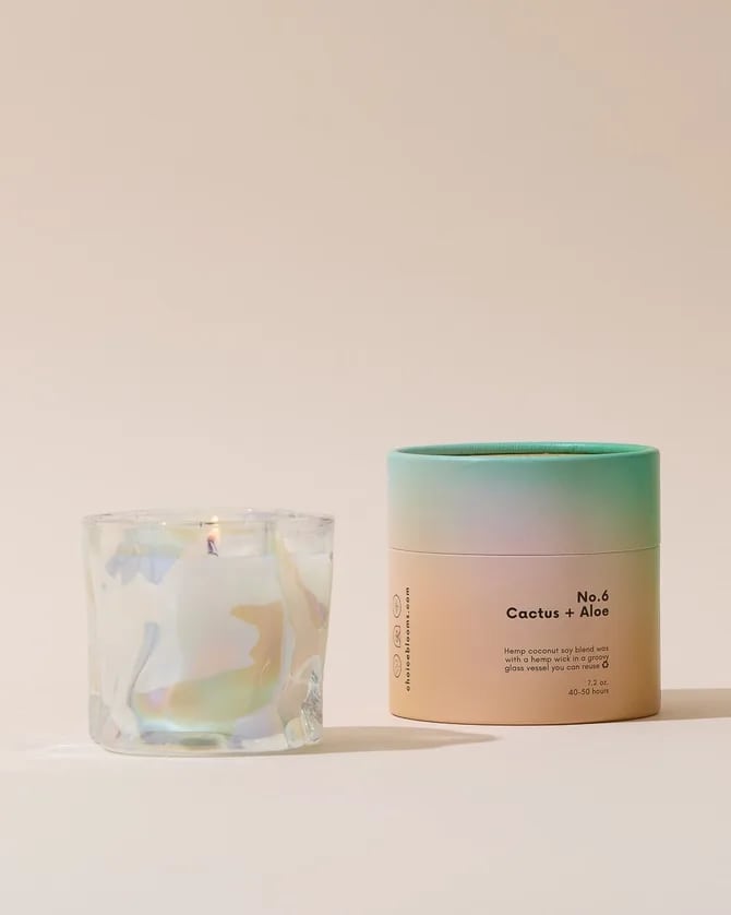 A scented candle in a glass jar beside its pastel cylindrical container