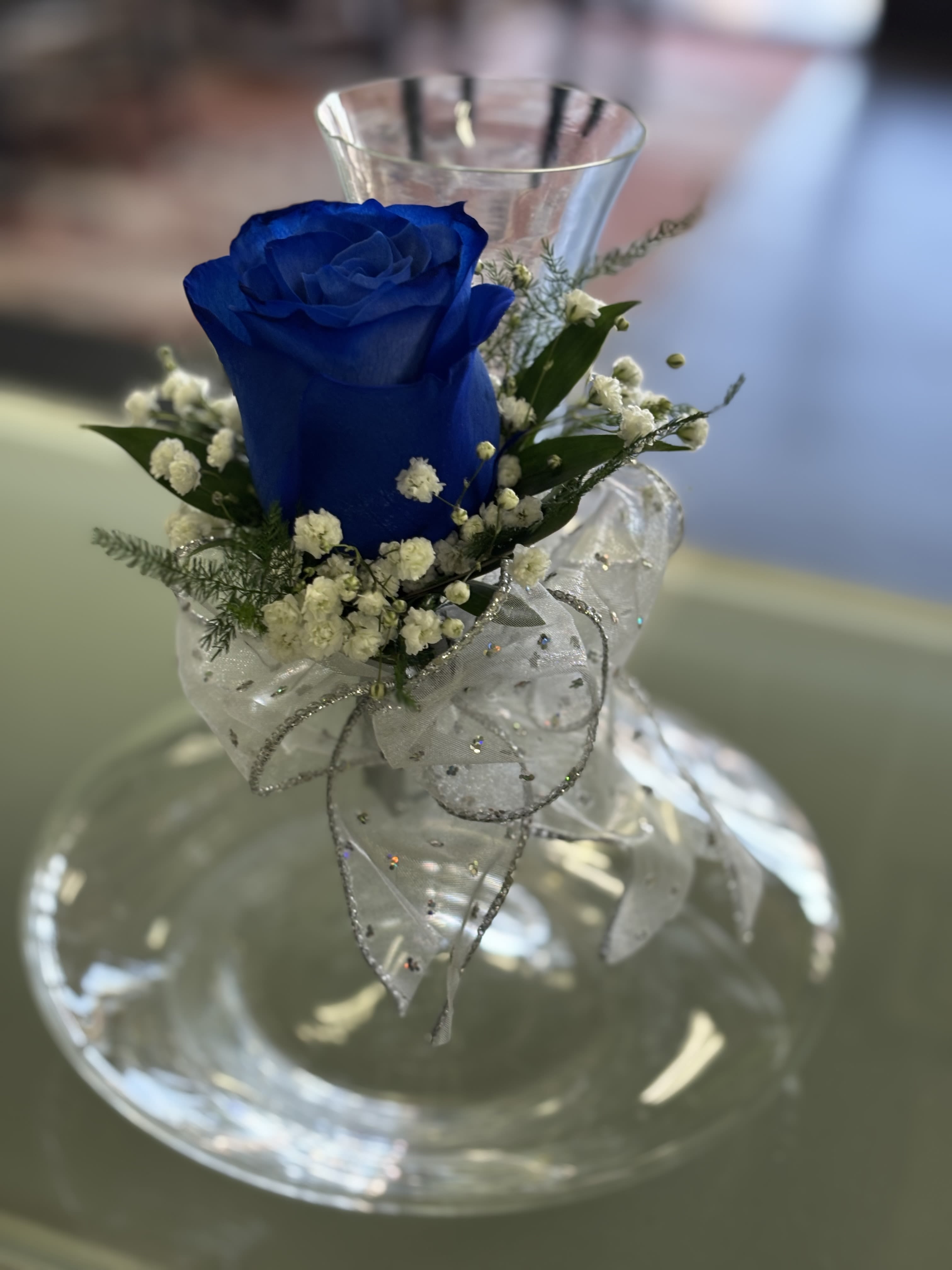 Single blue rose with white accent flowers and silver ribbon in a clear glass vase
