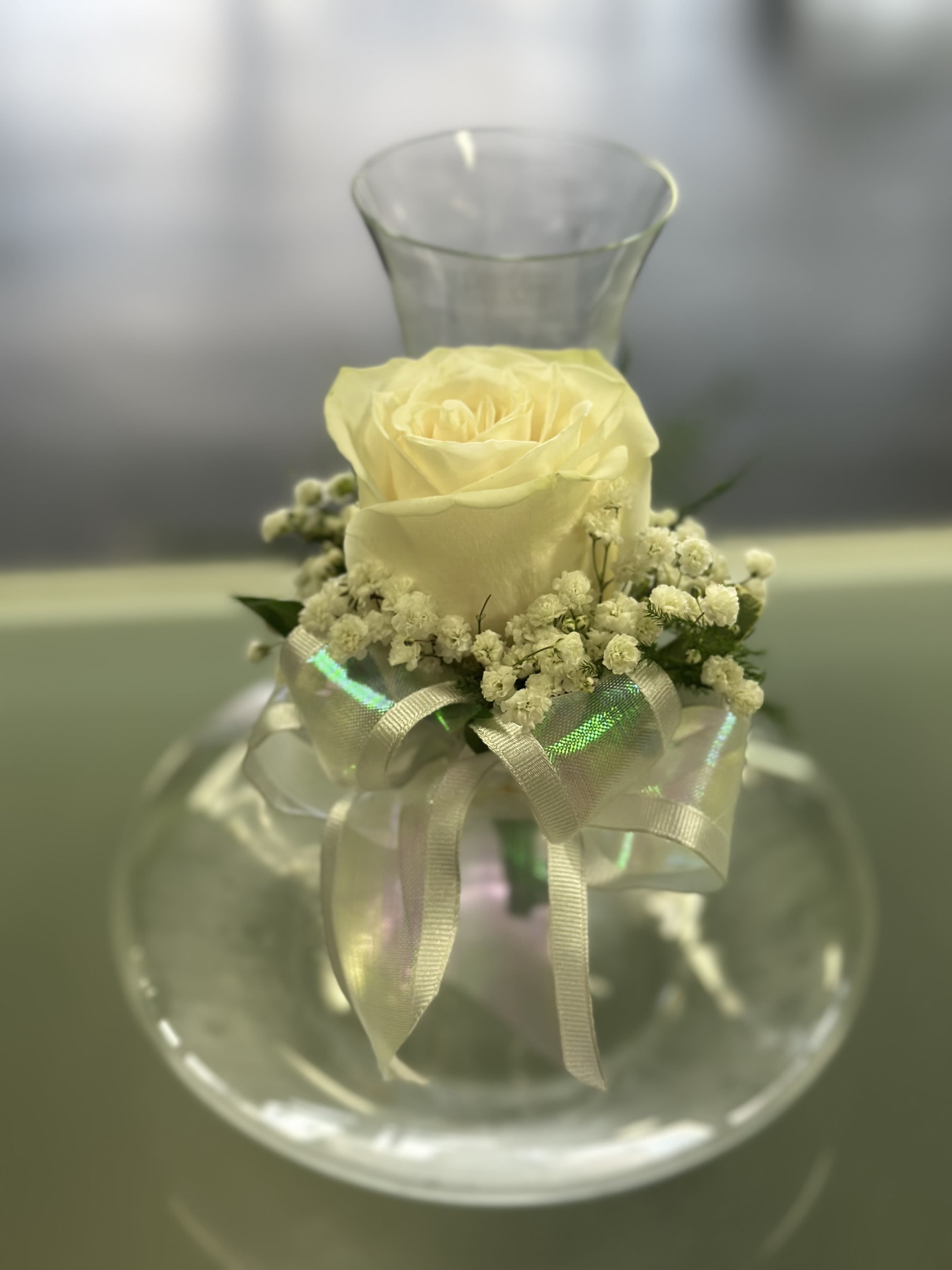 Single pale yellow rose in a clear glass vase with a ribbon bow