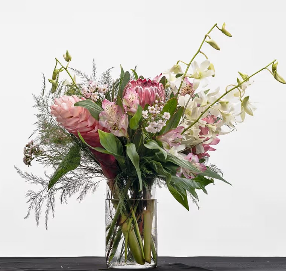 Barefoot Boujee - A vibrant tropical arrangement featuring a curated blend of pink blooms and lush greenery.   Soft and vivid pink flowers are thoughtfully layered with tropical textures to create a balanced composition that feels both luxurious and effortlessly natural. With its fresh color palette and modern tropical style, this arrangement brings a sense of warmth, sophistication, and coastal charm to any setting.