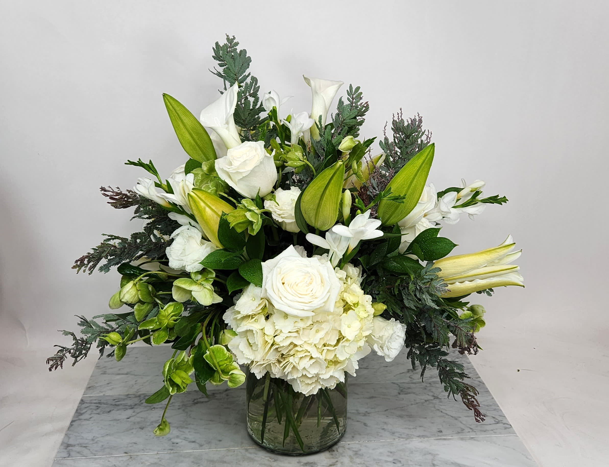 White floral arrangement with lilies, roses, and hydrangea in a glass vase
