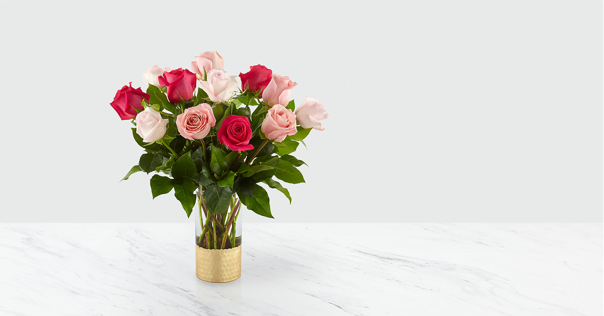 Pink and red roses arranged in a clear vase with a gold sleeve