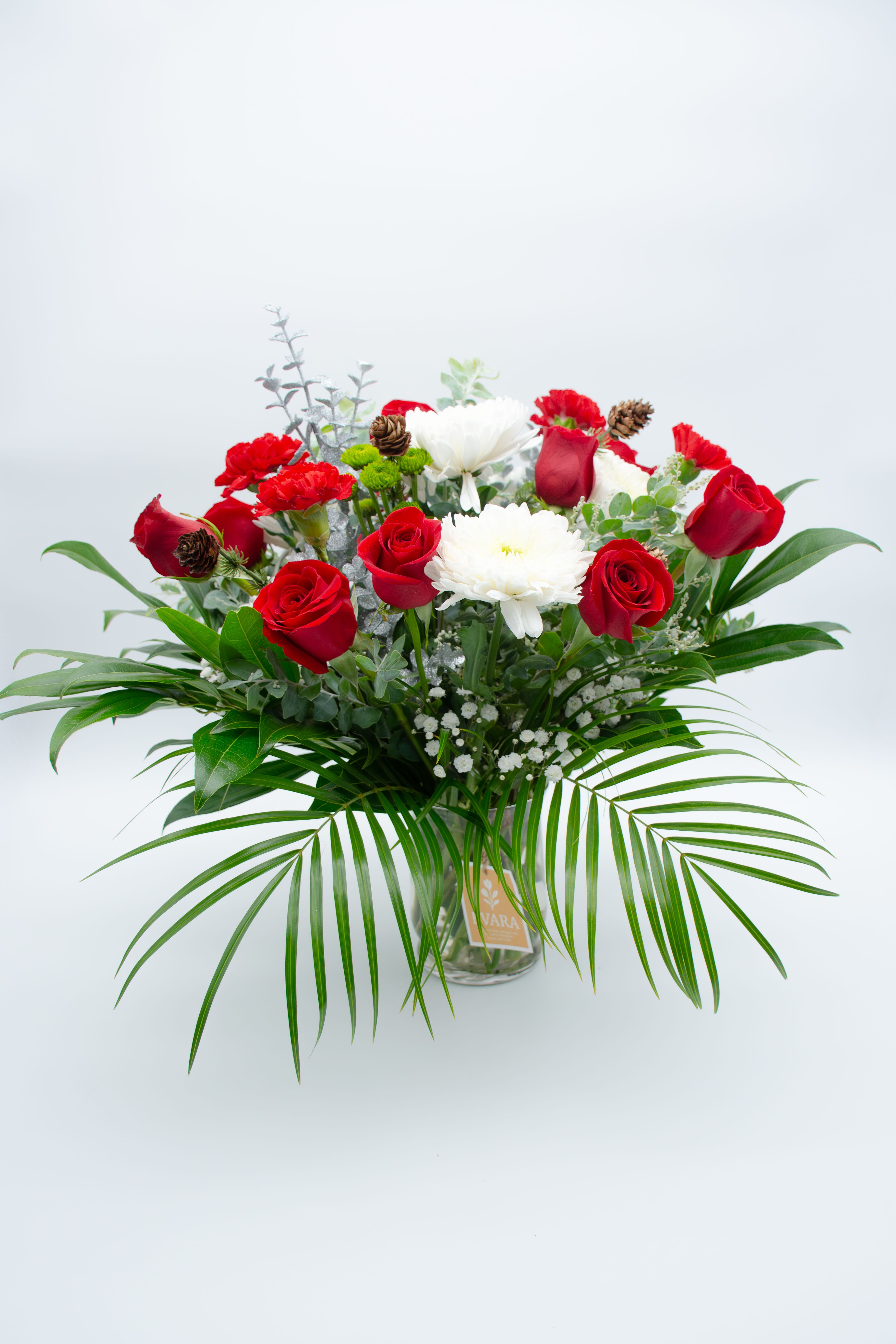 Red roses and white blooms in a glass vase with palm fronds