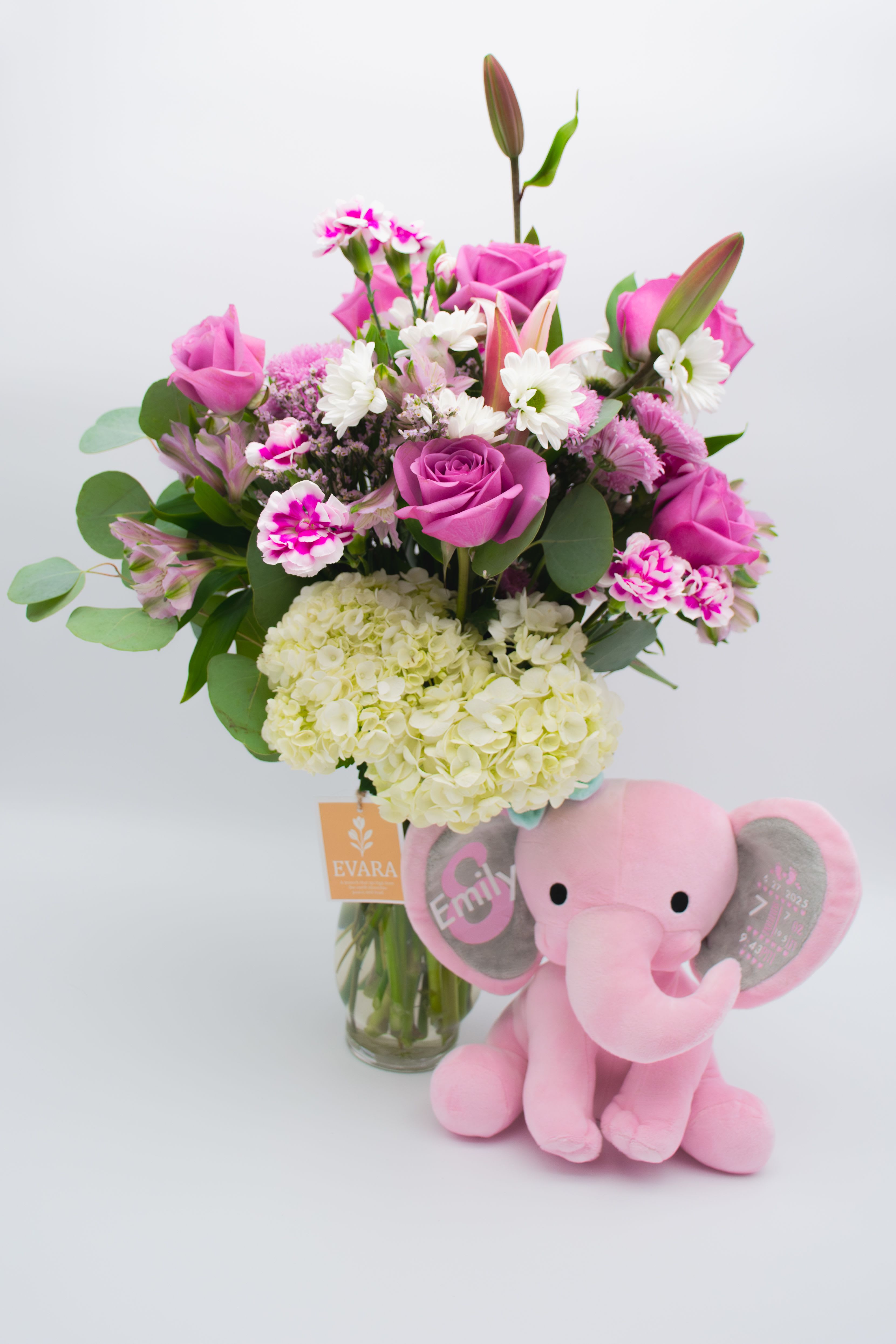 Pink rose bouquet in a glass vase with a plush pink elephant