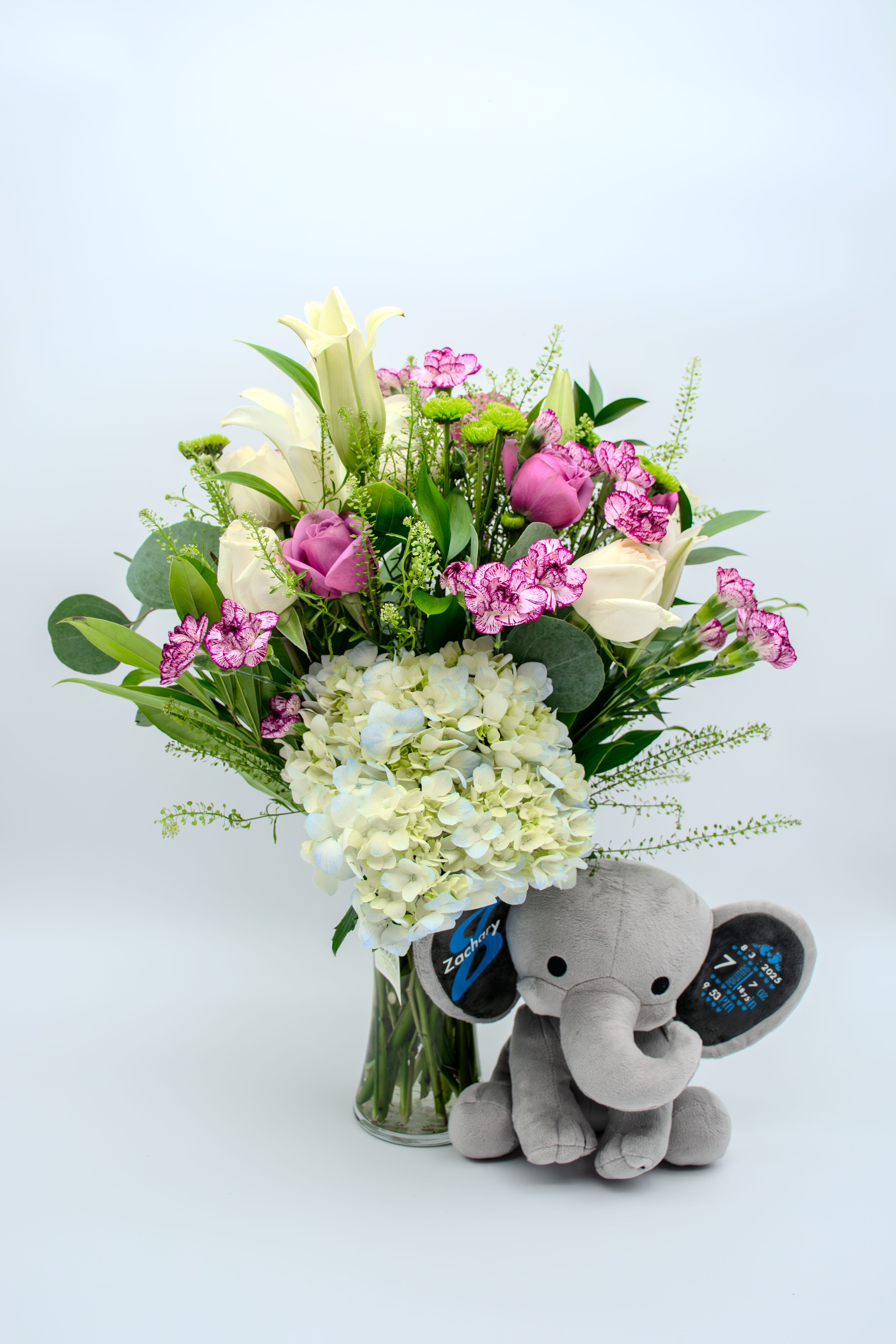 Bouquet of white and pink flowers in a glass vase with a gray plush elephant