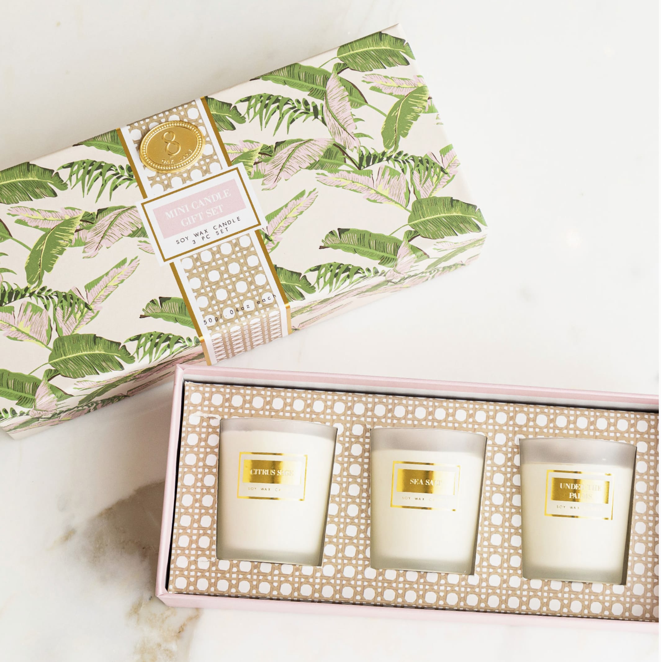 Three scented candles in a pink gift box with tropical-patterned packaging.