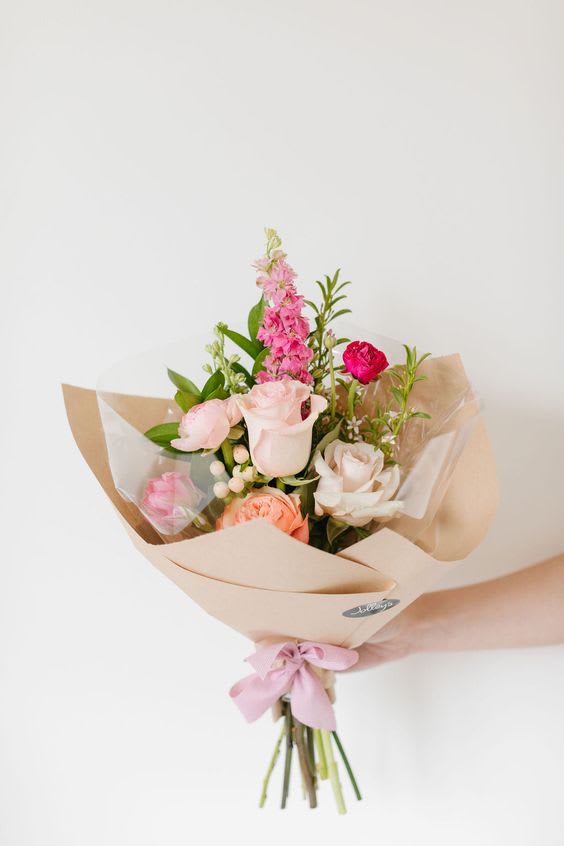 Hand-tied bouquet of pink and white roses wrapped in beige paper