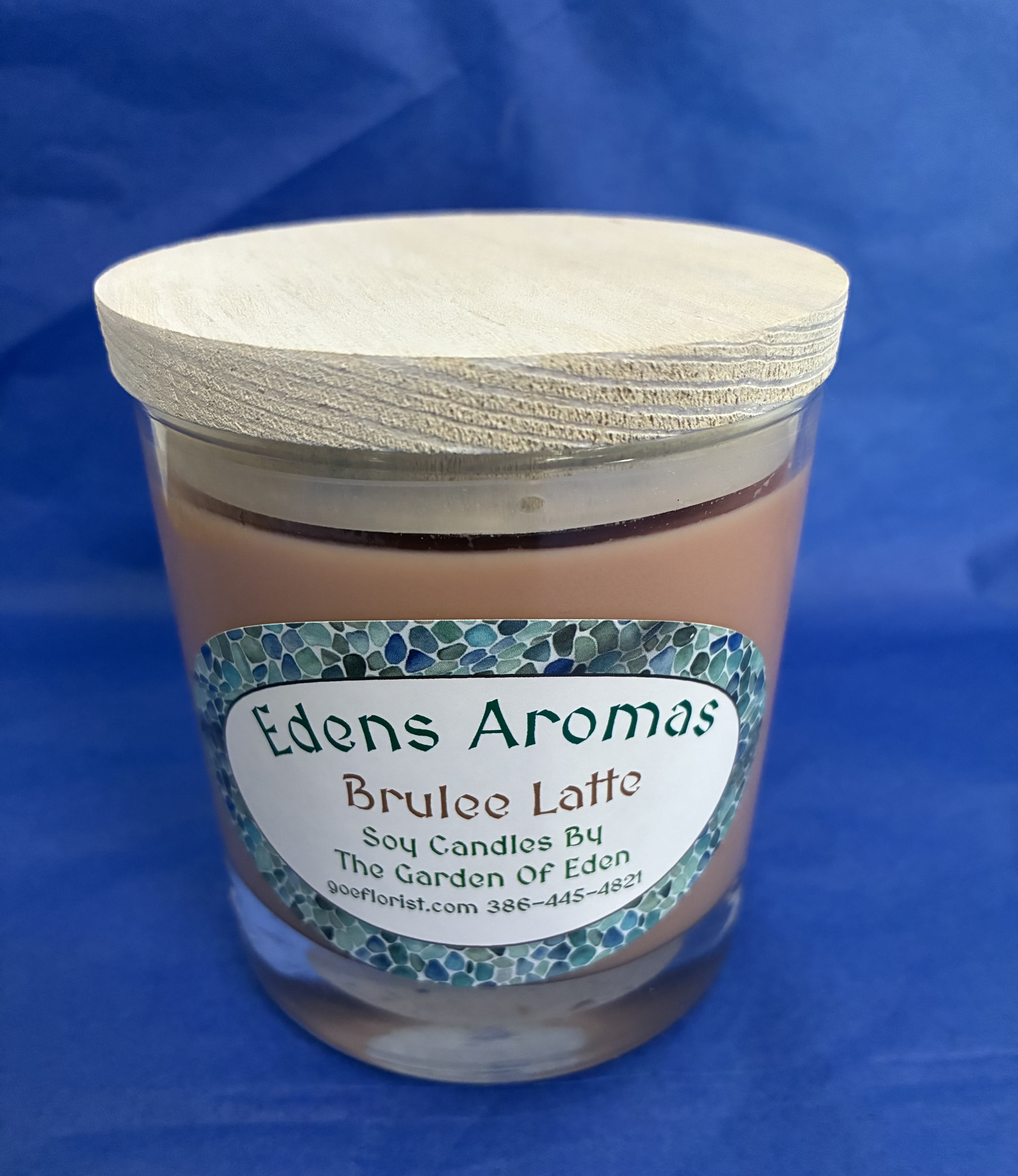Tan soy candle in a glass jar with light wooden lid and decorative label on a blue background