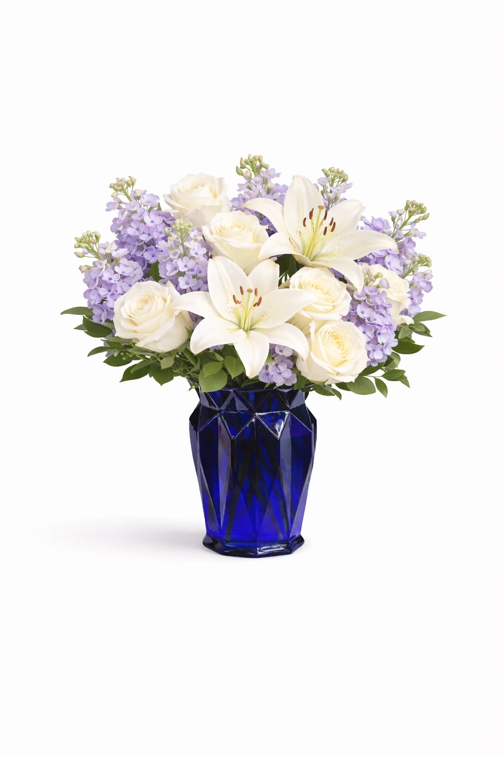 Serene Lavender Garden Arrangement - A refined and elegant floral arrangement featuring premium white roses, fragrant lavender stock, and graceful white lilies, beautifully designed in a modern cobalt blue vase. Accented with fresh seasonal greenery, this design offers a sophisticated balance of texture, color, and natural volume.  The combination of soft lavender tones and classic white blooms creates a timeless and calming aesthetic, making it an ideal choice for more meaningful and refined occasions.  Perfect for: sympathy, get well, thank you, thinking of you, and elegant everyday gestures.  Each arrangement is handcrafted using fresh, high-quality flowers. Bloom varieties may vary slightly based on seasonal availability while maintaining the overall style, color palette, and fullness.