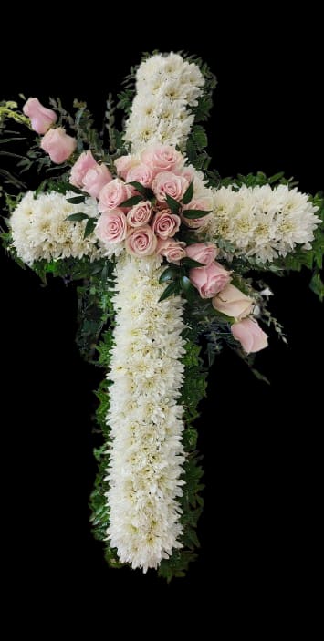 Graceful Farewell - A serene floral cross crafted for sympathy and funeral services, this arrangement places a dense bed of white chrysanthemums in a formal cross shape with a soft cluster of pale pink roses at the center. The white, pink, and green palette reads reverent and comforting-an appropriate tribute when you want the person you're thinking of to feel honored and remembered.  Dark green foliage outlines the cross and provides crisp contrast to the white chrysanthemum face and blush rose focal point, emphasizing the symmetrical, traditional silhouette. The compact, thoughtfully arranged blooms present a tidy, polished look suitable for chapel display or graveside service; care is minimal-keep out of direct heat and mist lightly if needed to maintain freshness during services.