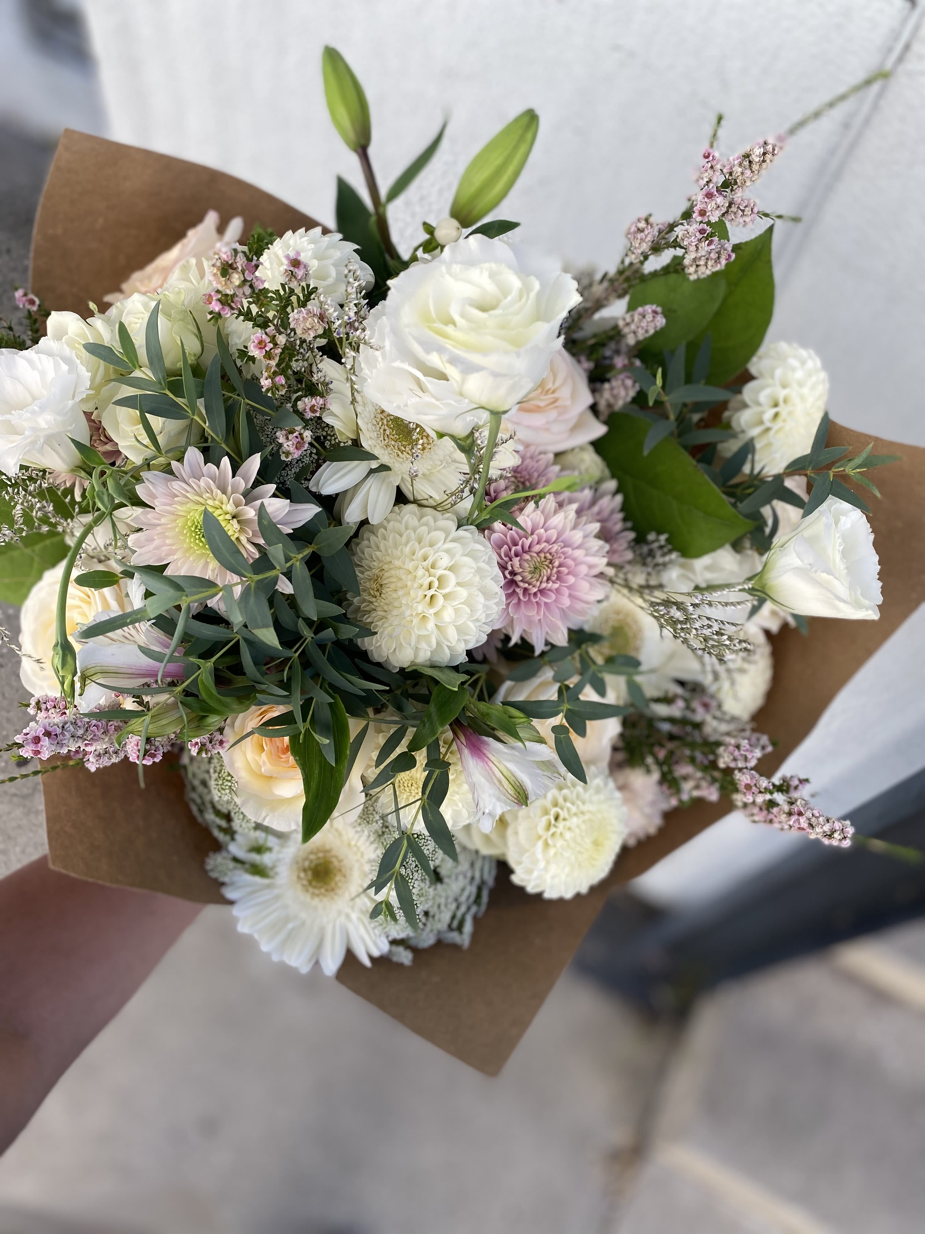 Hand-tied bouquet of white and blush flowers wrapped in brown paper